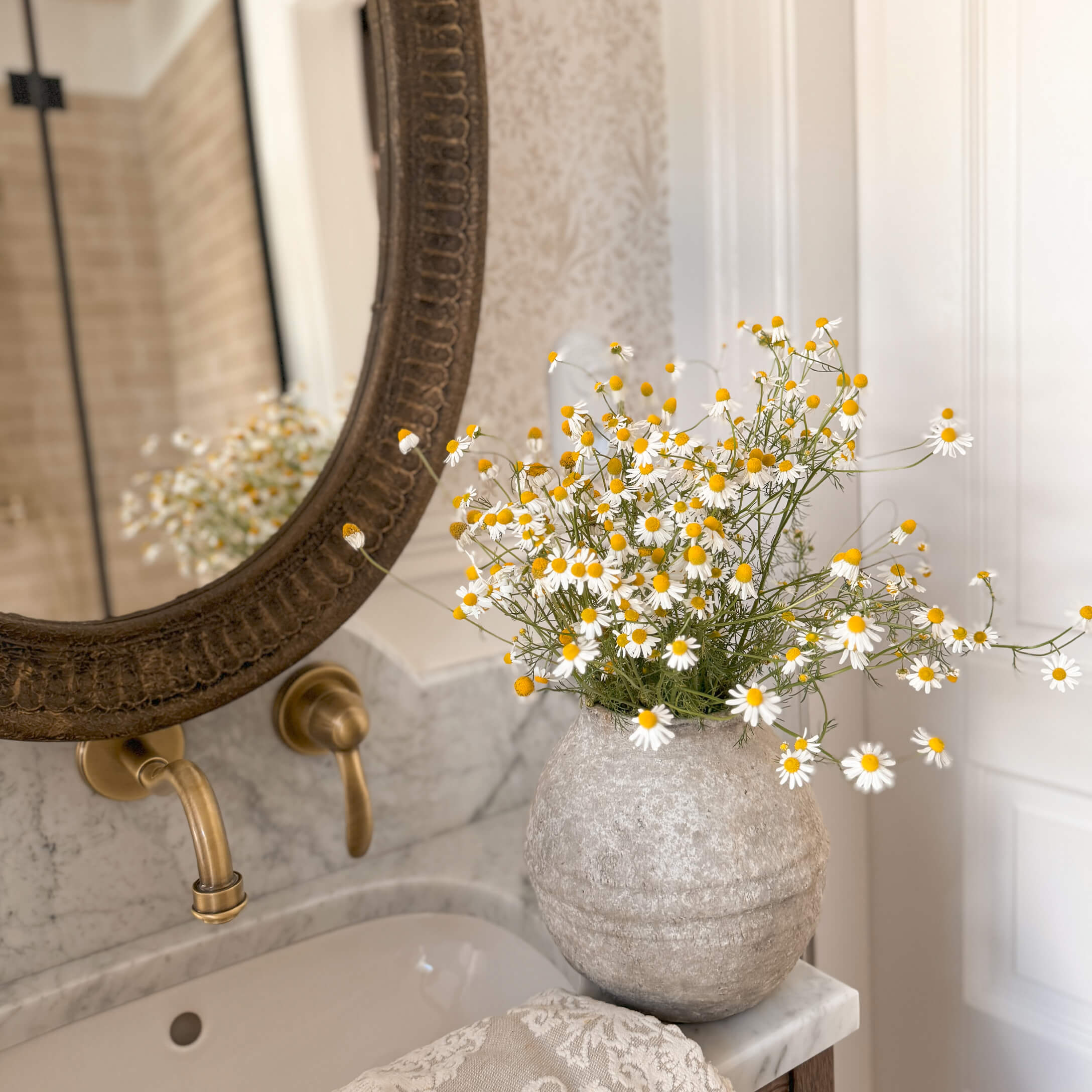 Vase en pierre grise avec fleurs blanches et jaunes sur un lavabo en marbre dans une salle de bain élégante