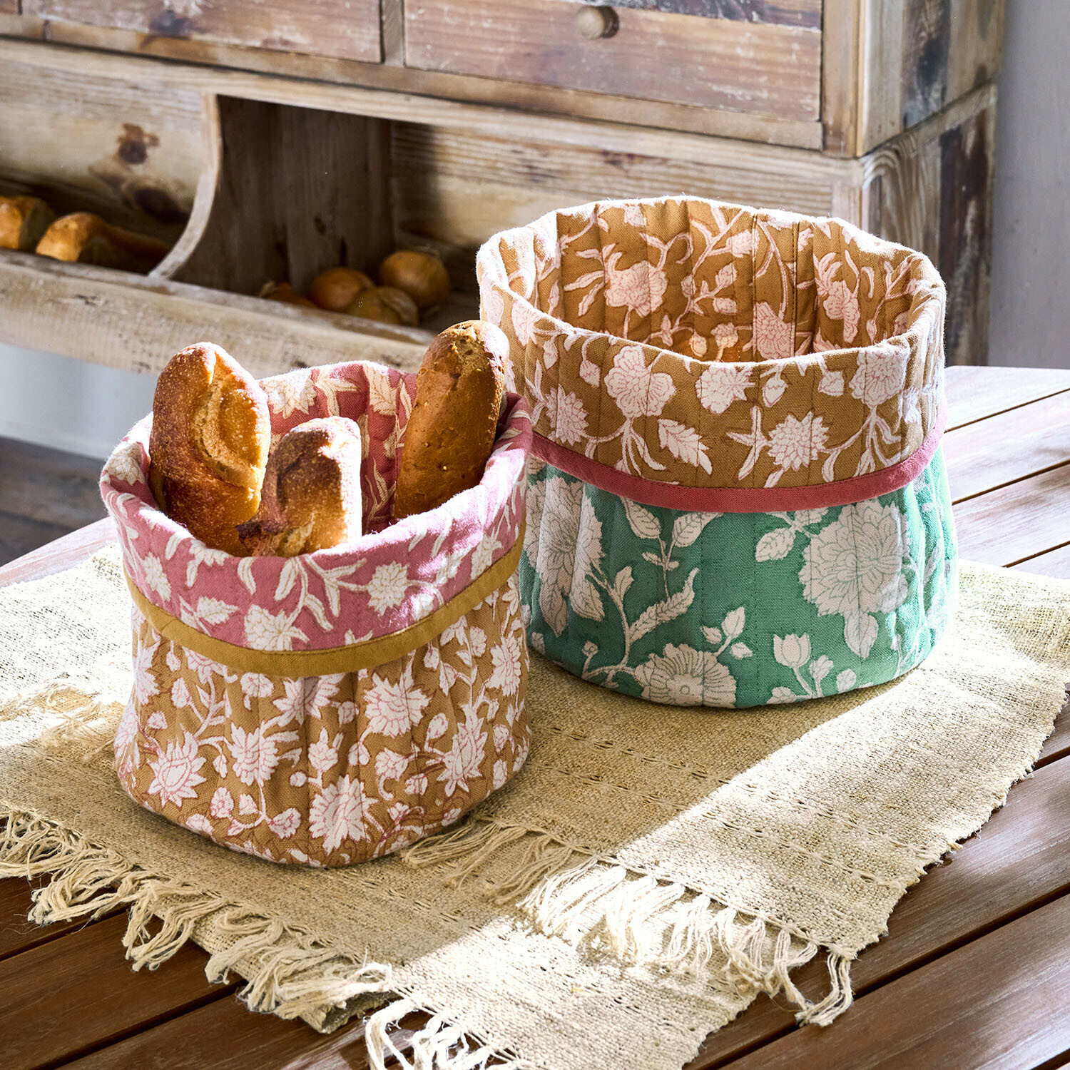 Lot de 2 paniers Fleuronnes Deux paniers en coton décoratifs à motif floral rose, marron et vert pour le pain sur une table en bois
