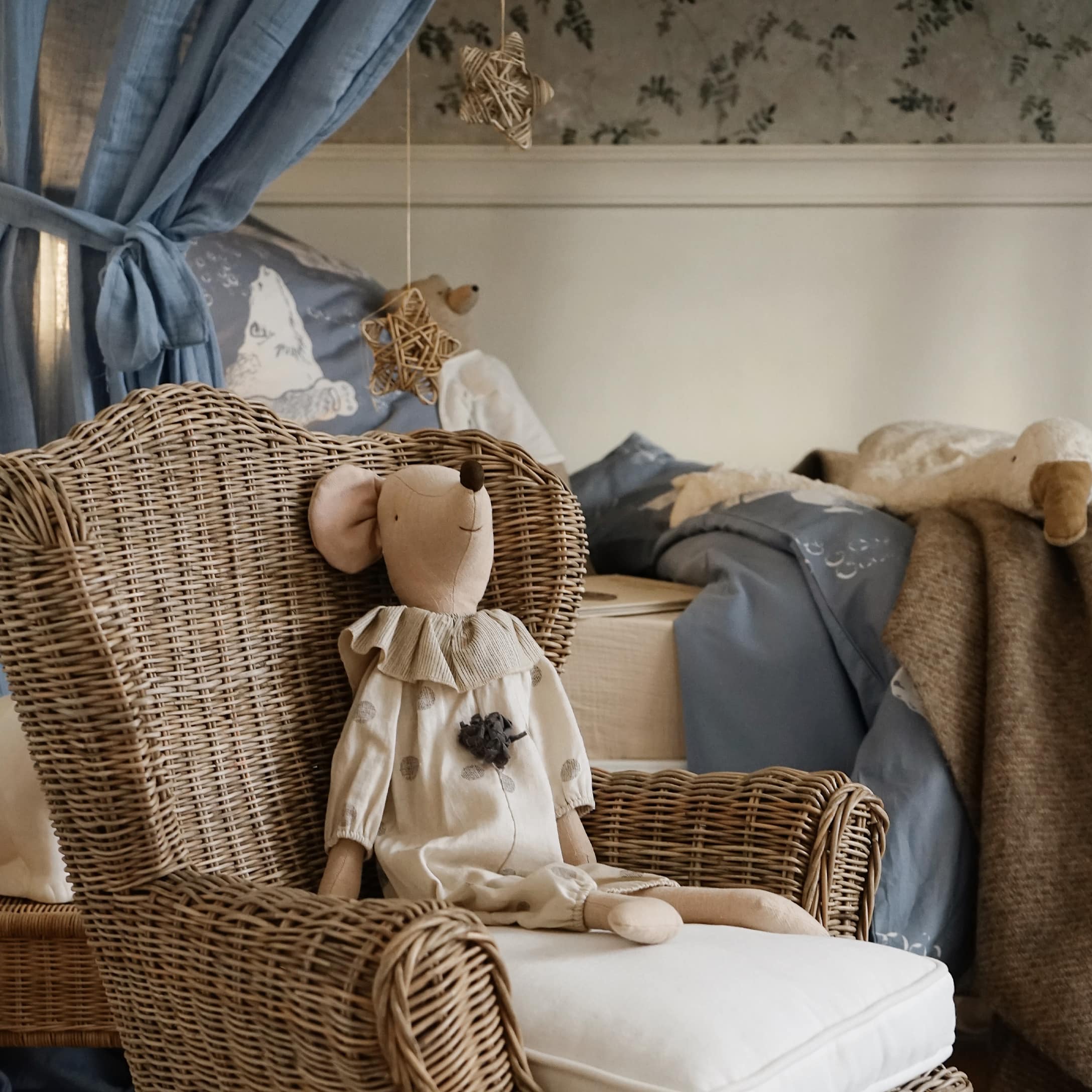 Fauteuil en osier naturel avec coussin clair et souris en peluche beige dans une chambre d'enfant