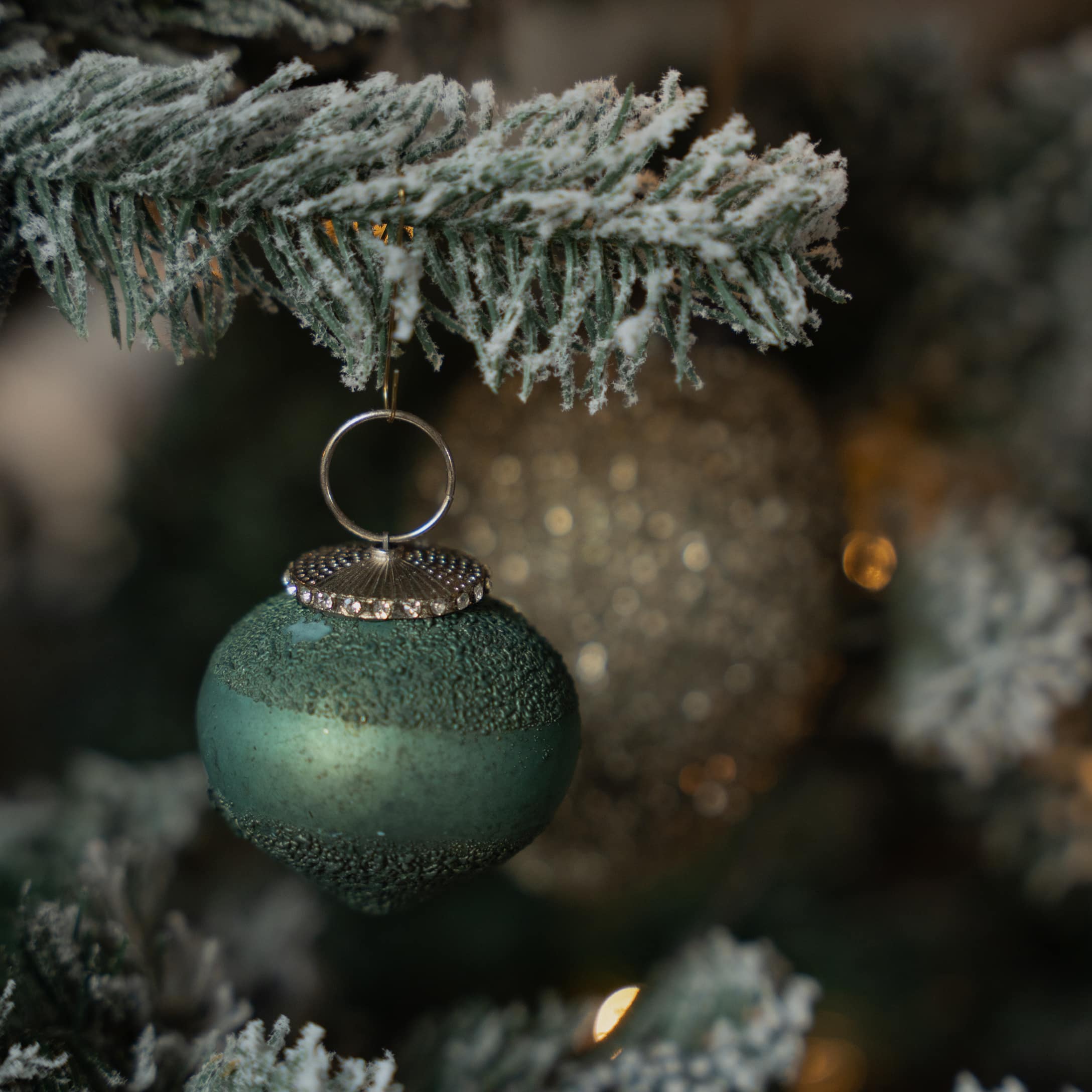 Boule de Noël verte mate avec attache métallique suspendue à une branche enneigée d'arbre de Noël