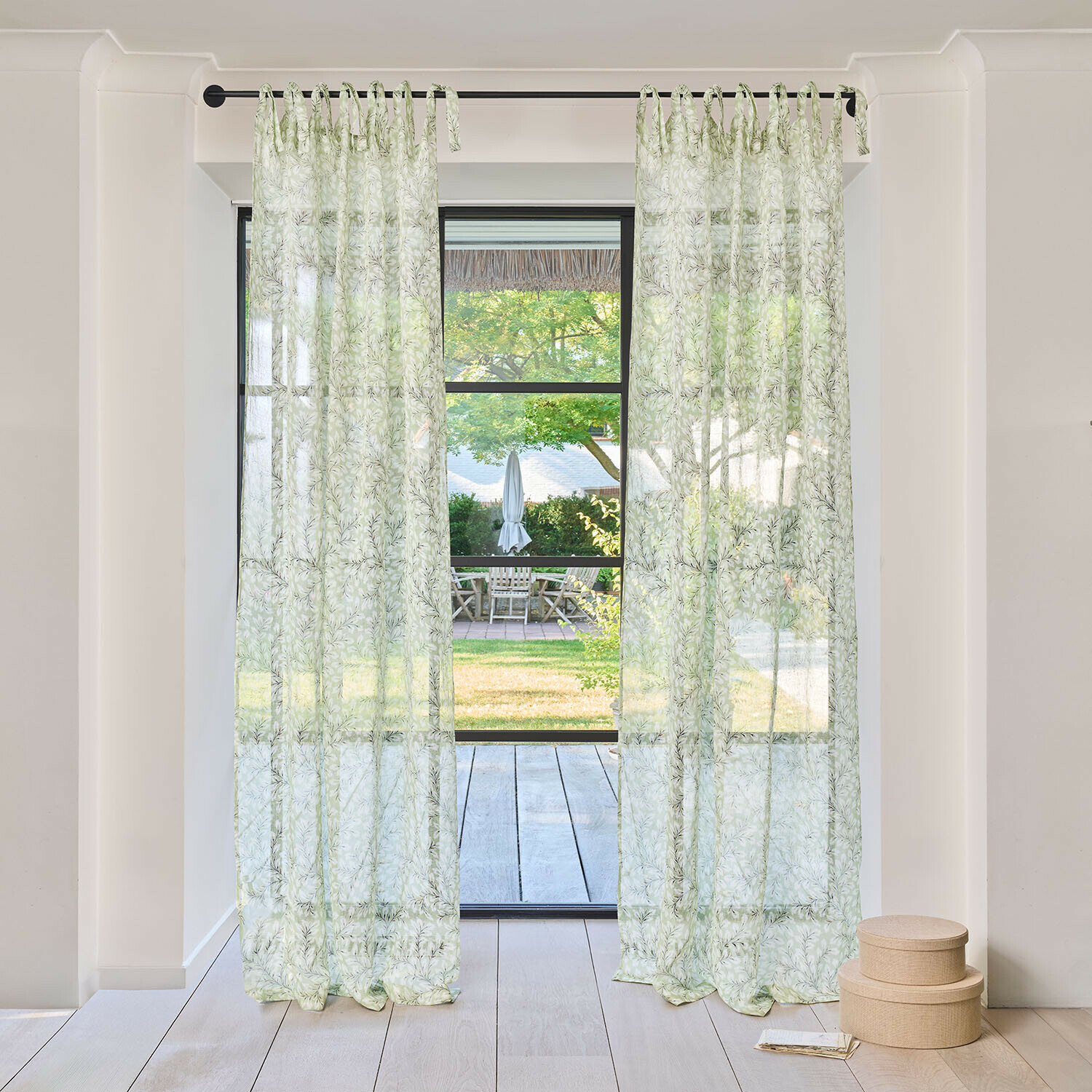 Rideau Norelline Rideaux transparents à motif de feuilles vertes sur tringle noire dans une pièce lumineuse avec vue sur jardin