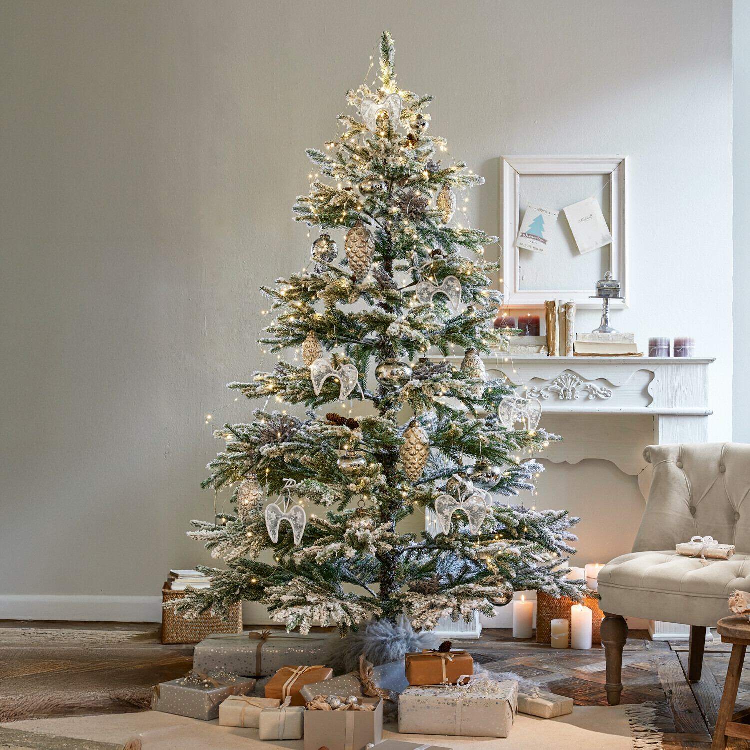 Sapin de Noël Lokossa Sapin de Noël enneigé décoré d'ornements blancs et dorés avec cadeaux près d'un fauteuil beige dans un salon cosy