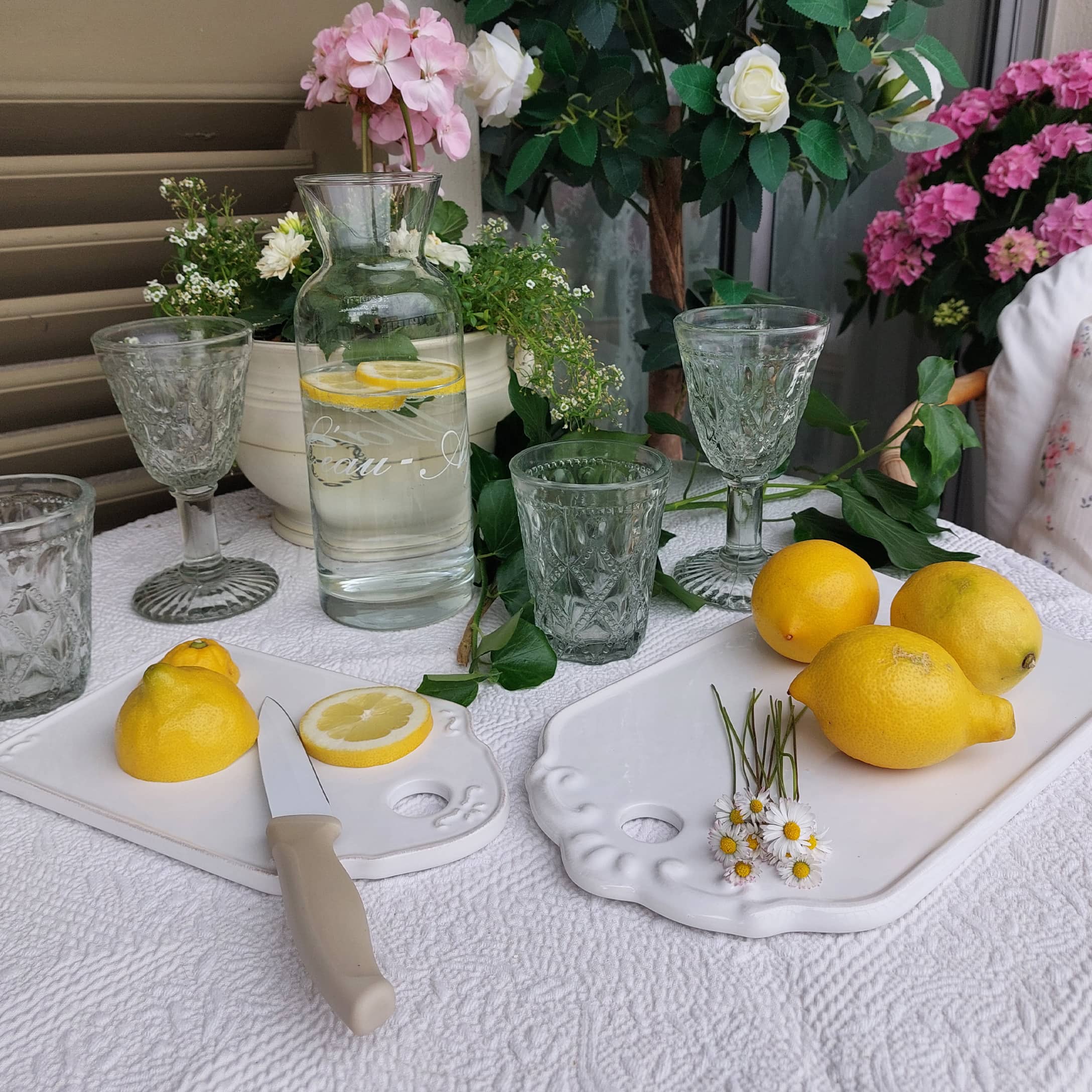 Carafe en verre avec eau citronnée sur nappe blanche, verres décoratifs et citrons jaunes