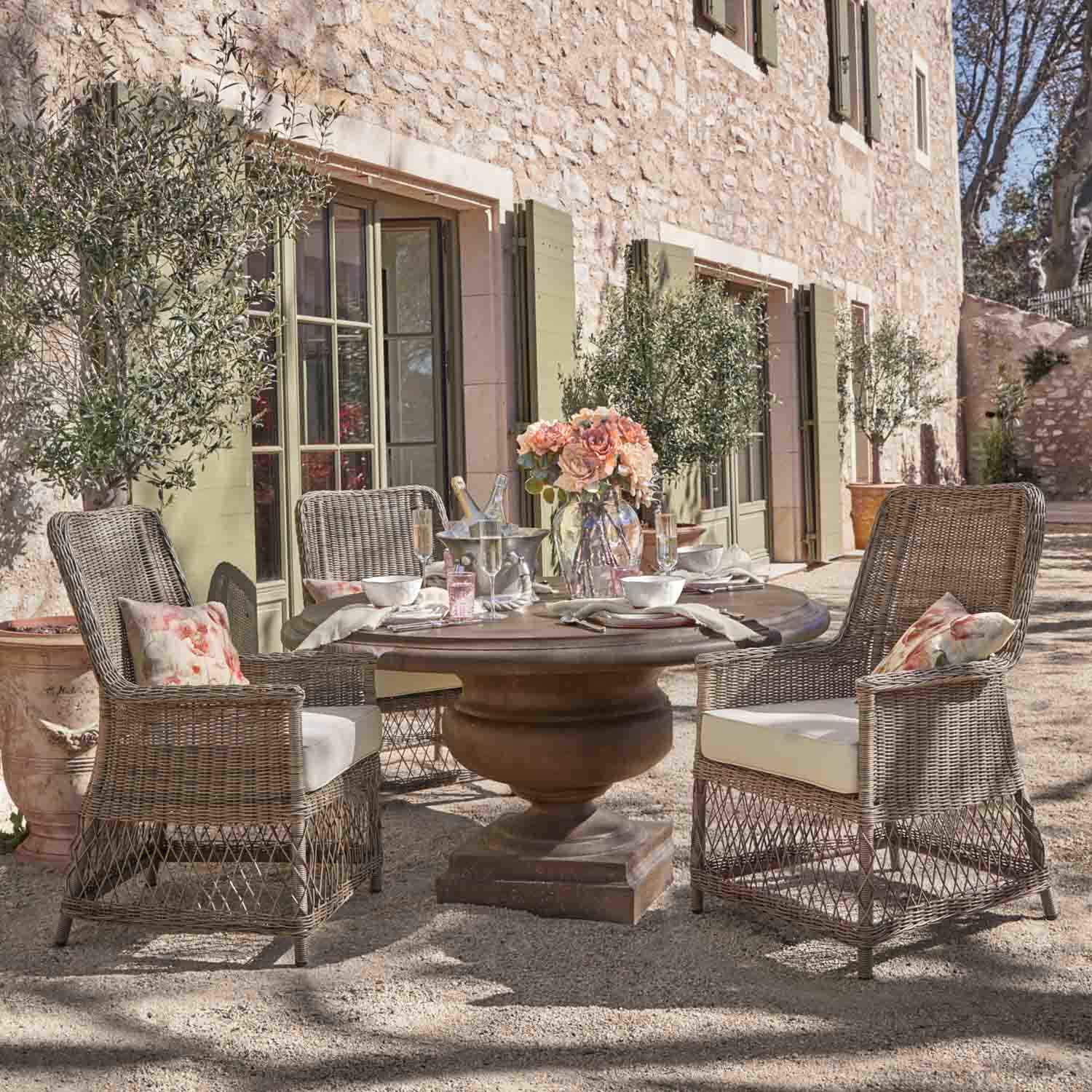 Table ronde en pierre avec chaises en osier et bouquet de fleurs sur terrasse extérieure ensoleillée
