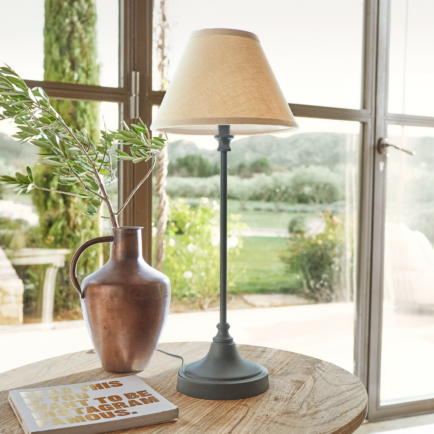 Lampe de table avec base en métal et abat-jour beige sur table en bois avec vase et livre