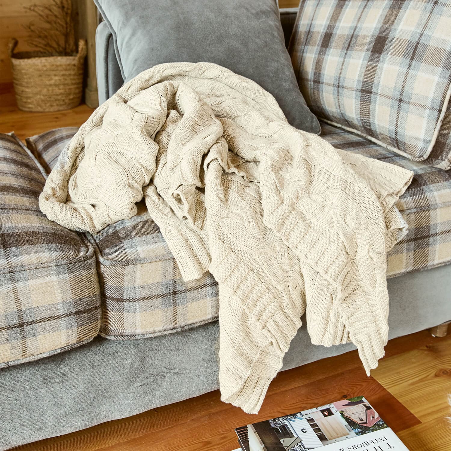 Plaid beige en tricot torsadé posé sur un canapé gris à carreaux beige dans un salon chaleureux