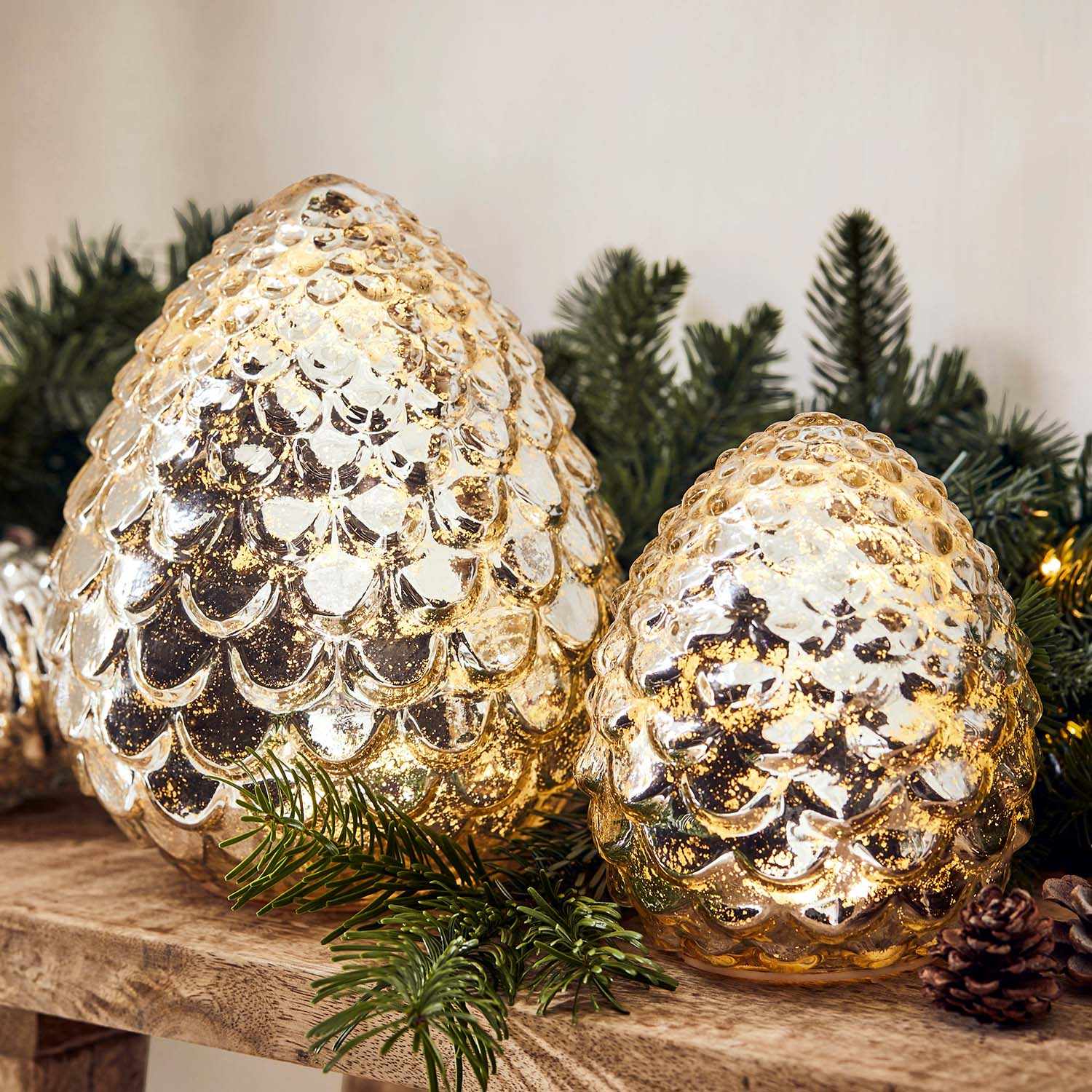 Décorations en verre doré en forme de pommes de pin sur une étagère en bois avec branches de sapin