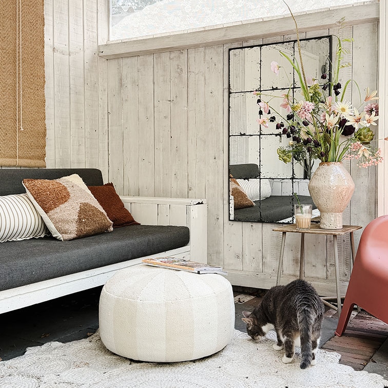 Salon cosy avec mur en bois blanc, canapé gris, pouf blanc et décor floral sur table en bois
