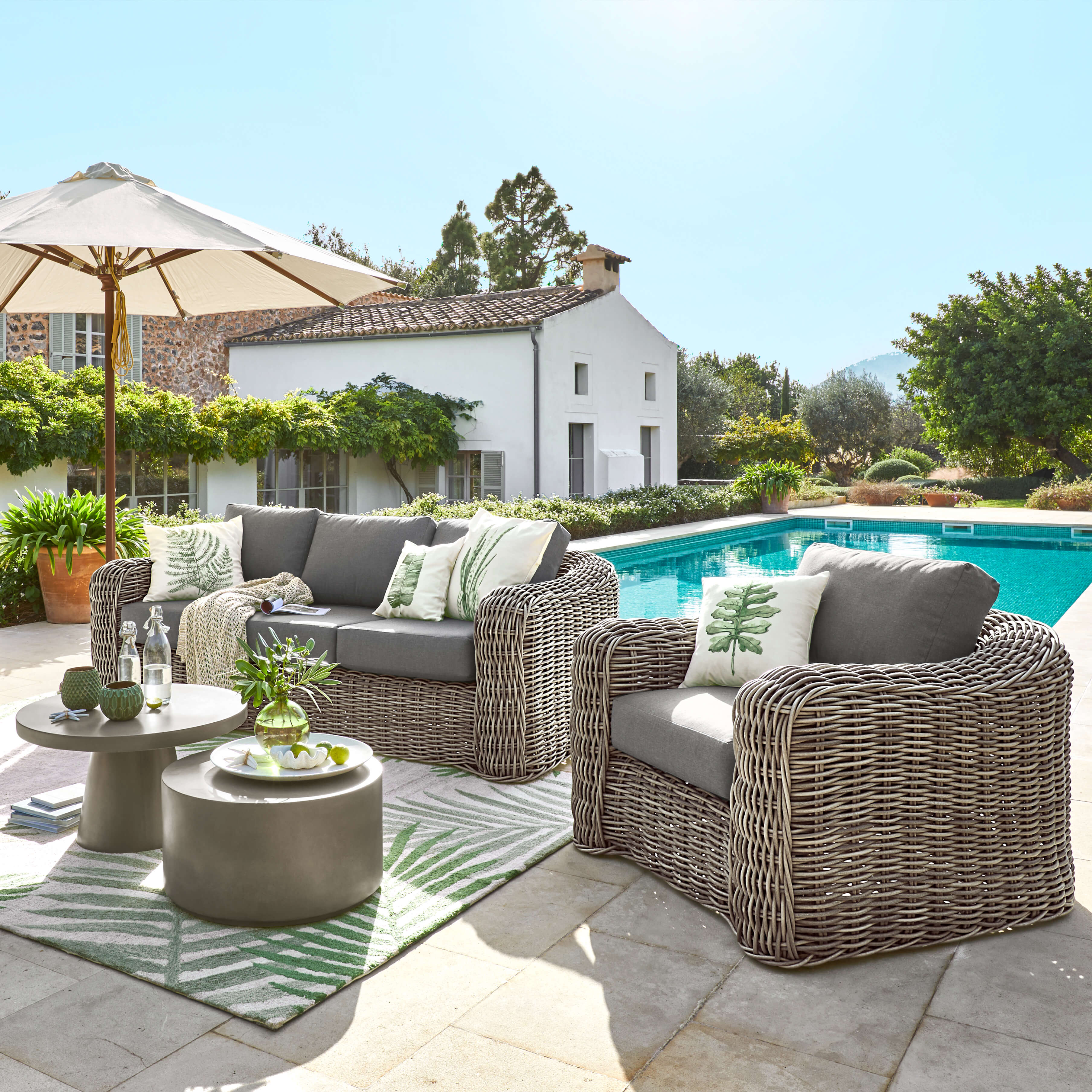 Ensemble de mobilier de jardin en rotin gris avec coussins et tables basses près de la piscine