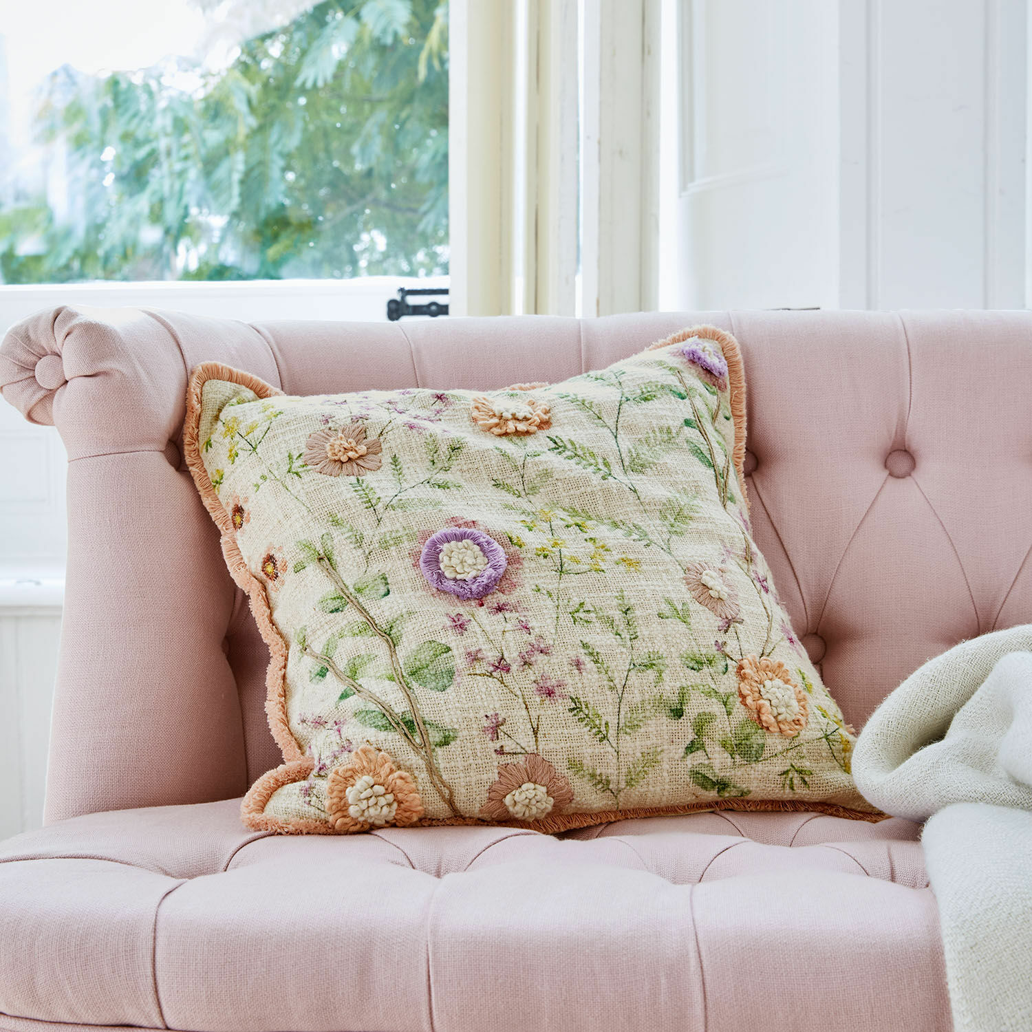 Housse de coussin Lailah Coussin décoratif brodé de fleurs sur un canapé rose capitonné dans un intérieur lumineux