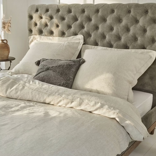 Linge de lit beige en lin sur lit avec tête de lit capitonnée grise, tissu naturel pour chambre