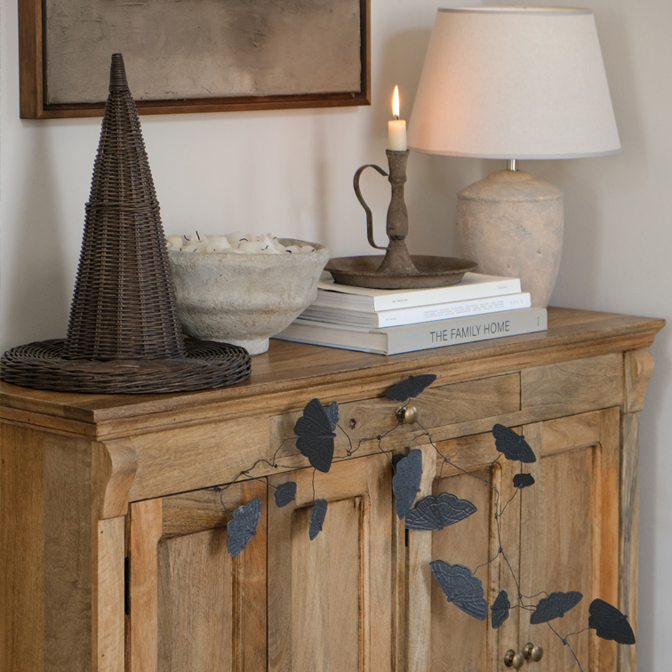 Buffet en bois avec guirlande de feuilles noires, lampe et bougeoir sur des livres dans un salon