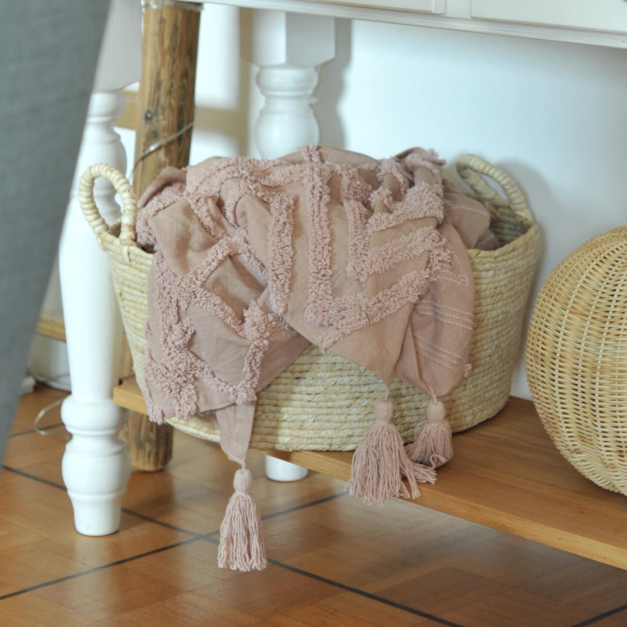 Plaid rose en coton avec pompons dans un panier en osier sur une étagère en bois