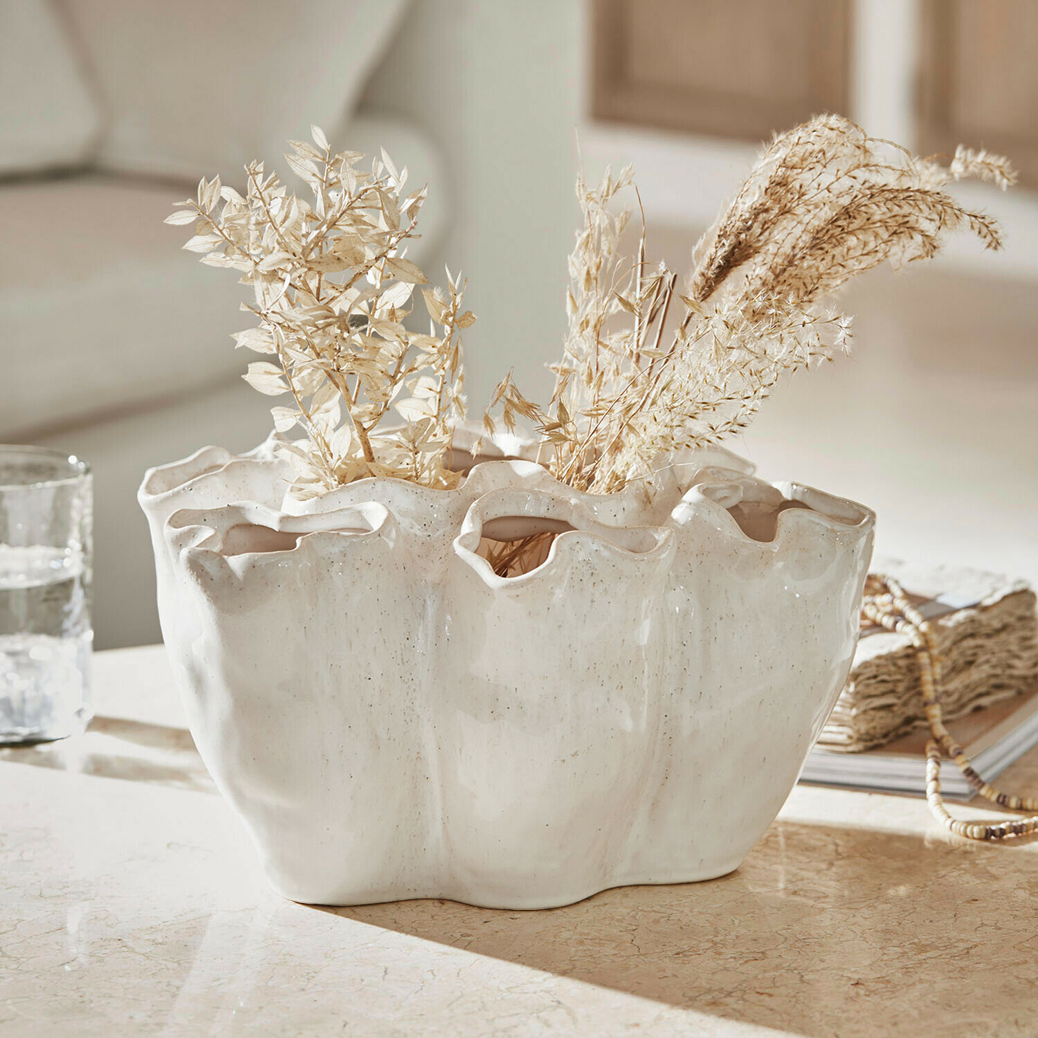 Vase Rovinia Vase en céramique blanche avec bord ondulé et plantes séchées sur une table décorative