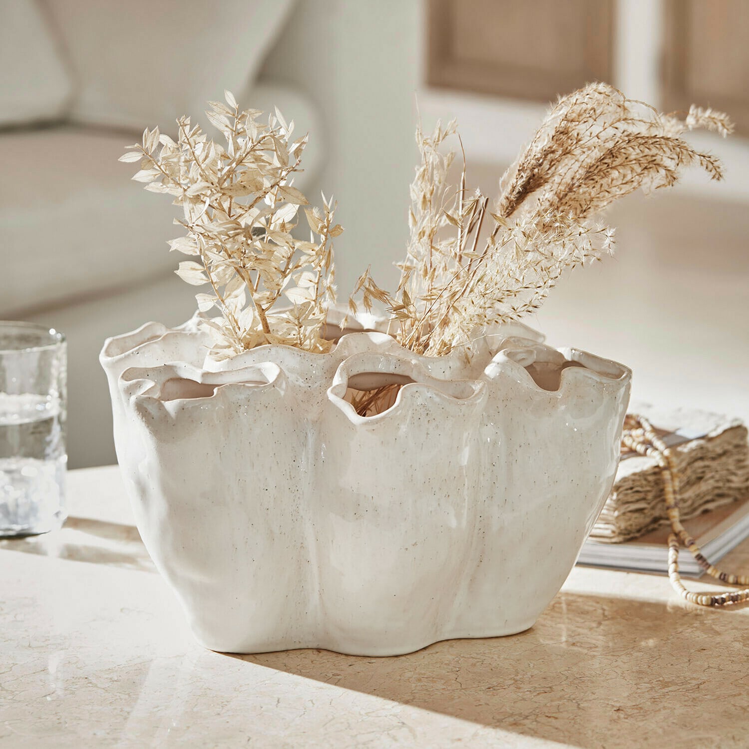 Vase Rovinia Vase en céramique blanche avec bord ondulé et plantes séchées sur une table décorative
