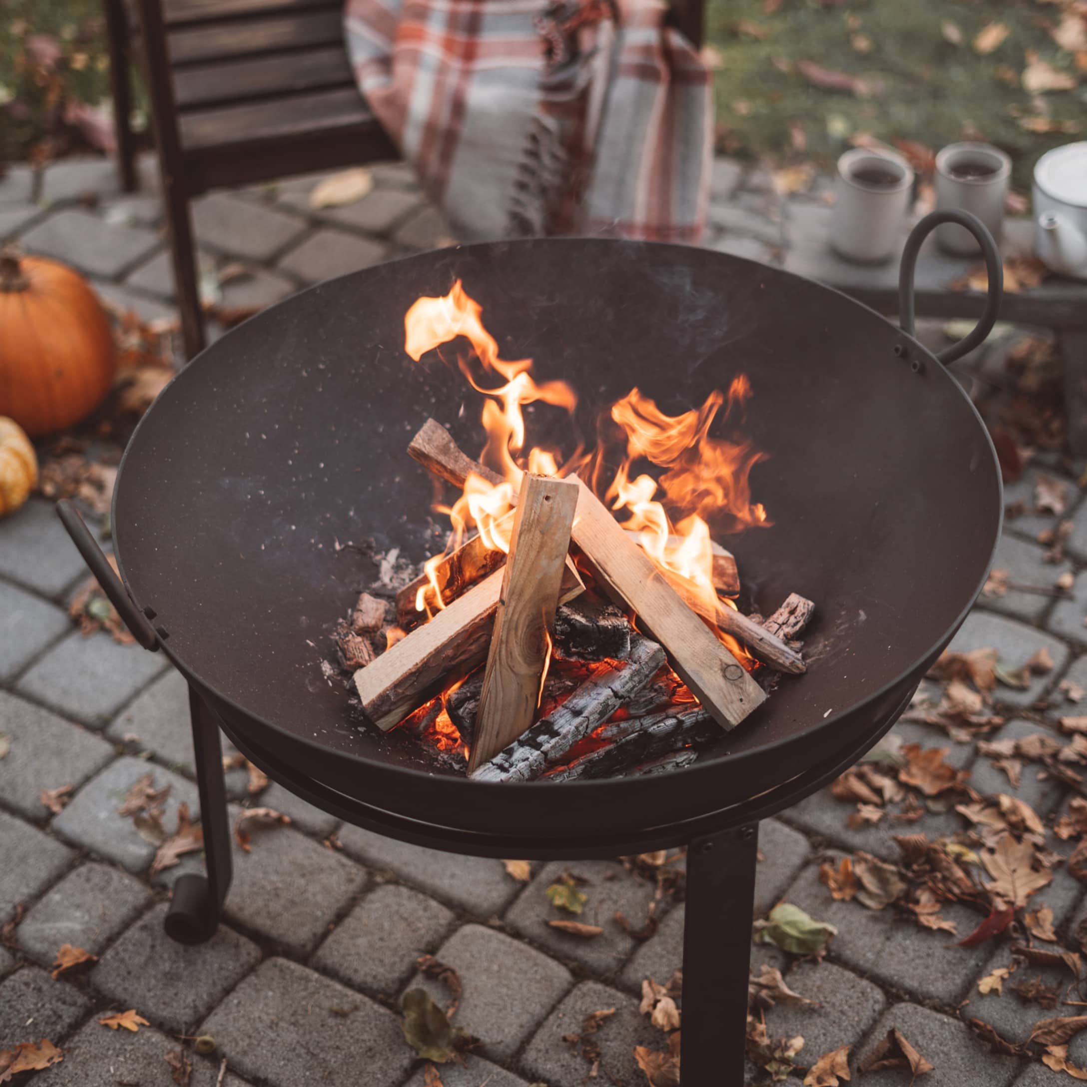Brasero de jardin noir en métal avec feu de bois allumé sur une terrasse pavée
