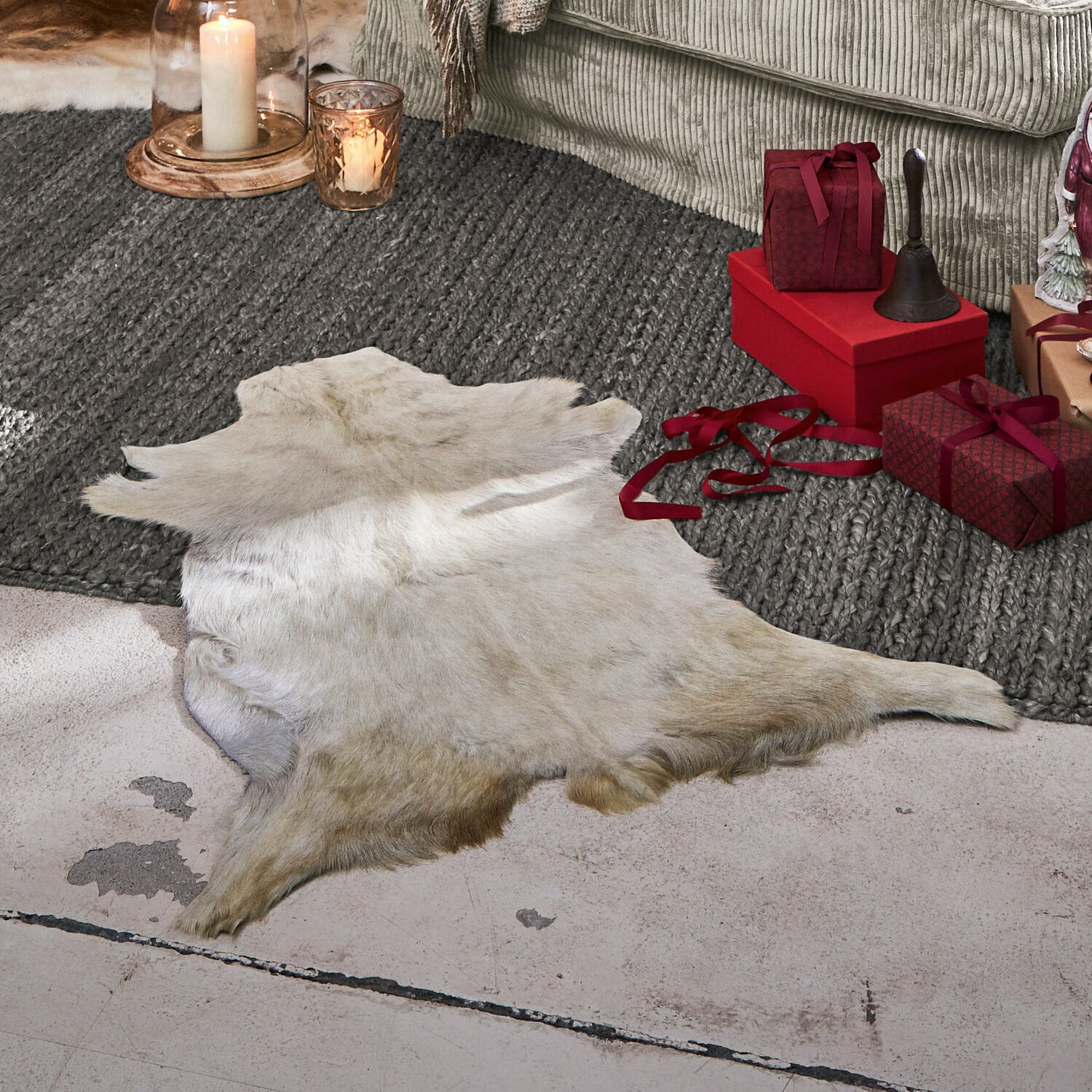 Peau de chèvre Piedro Peau d'animal blanche naturelle posée sur le sol près de cadeaux rouges et bougies dans un salon