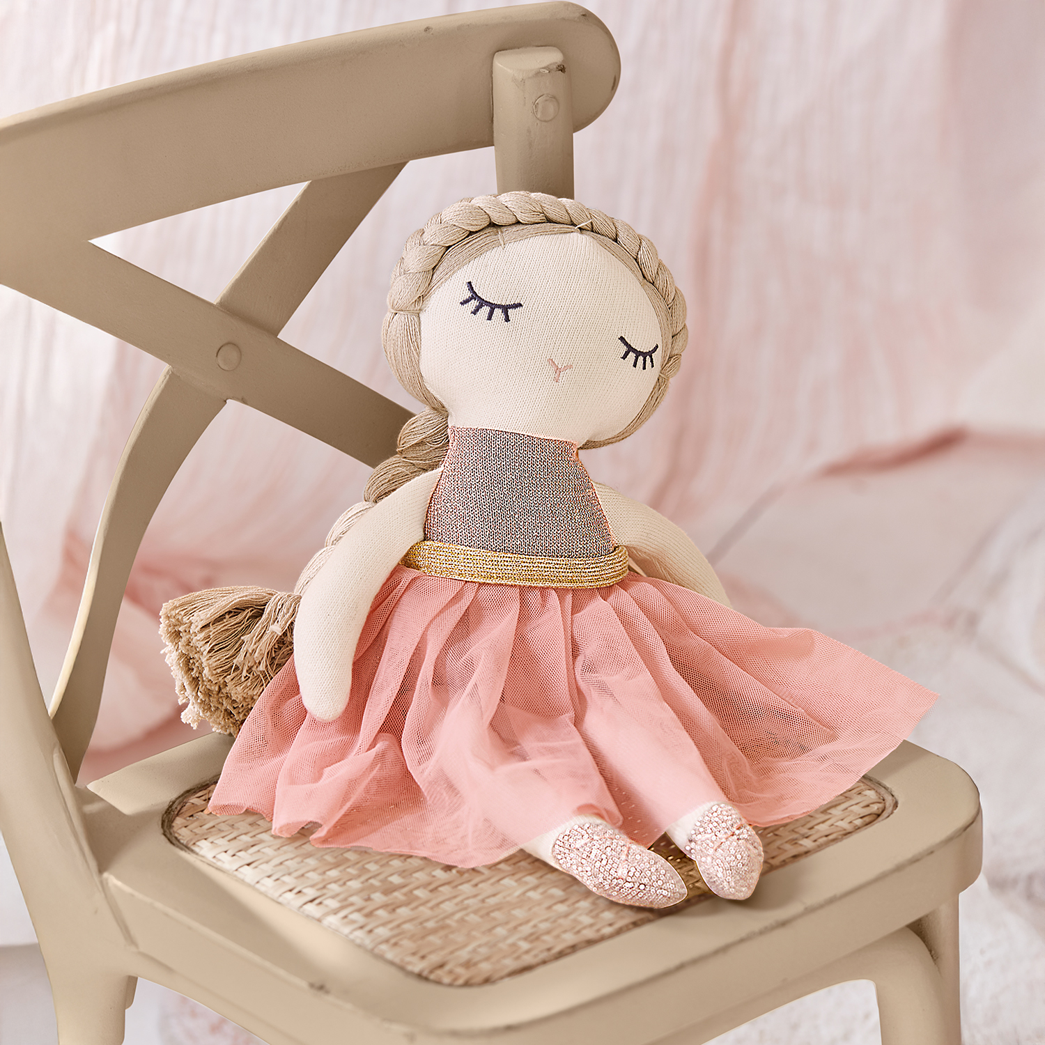 Poupée en tissu avec robe rose et ceinture dorée assise sur une chaise beige, jouet pour enfant