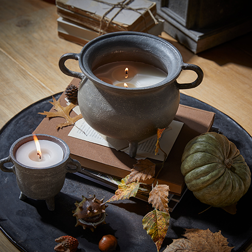 Bougie dans un récipient en céramique grise avec poignées sur une table en bois décorée d'éléments d'automne