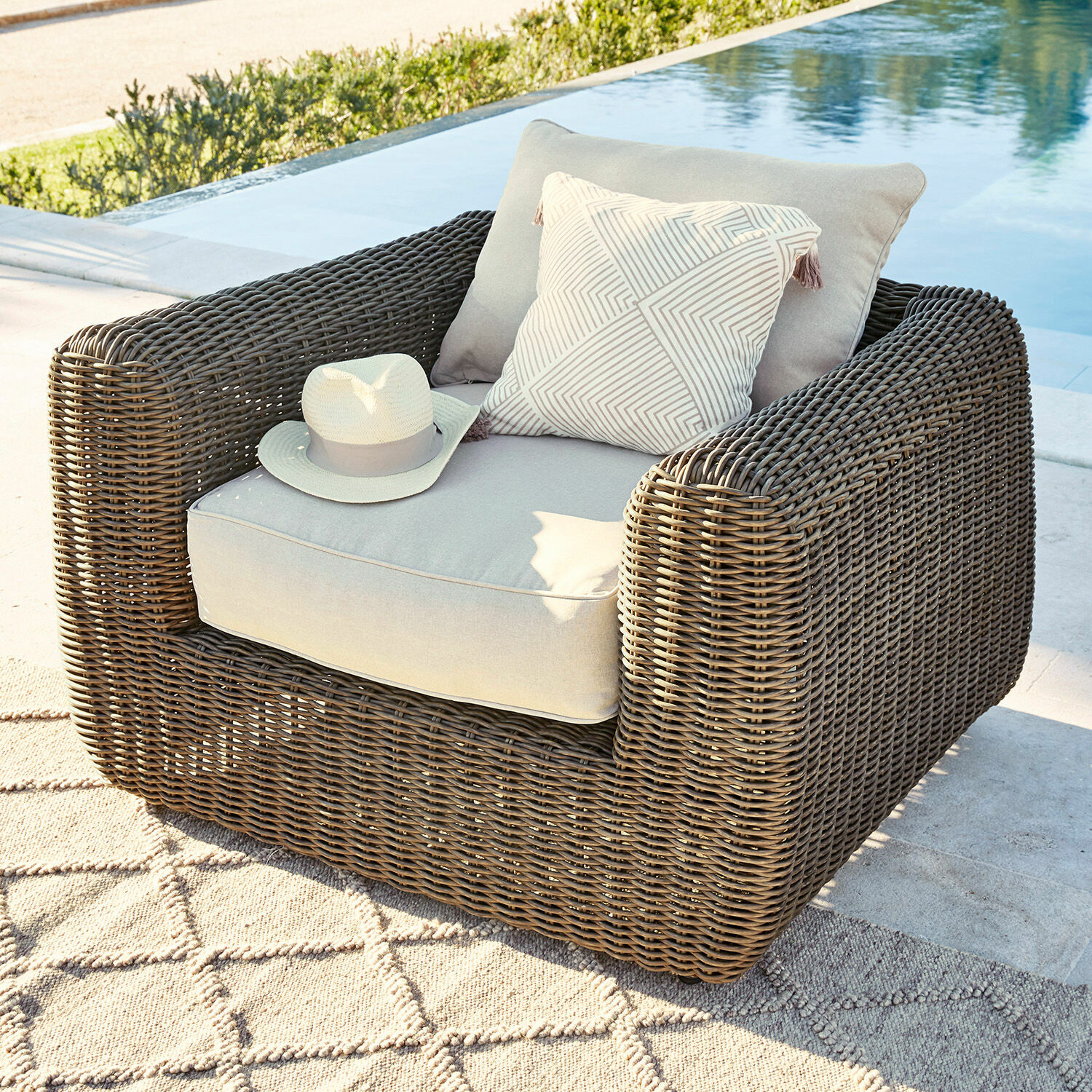 Fauteuil Bogdanne Fauteuil d'extérieur en rotin brun avec coussins gris clair et coussin décoratif près de la piscine
