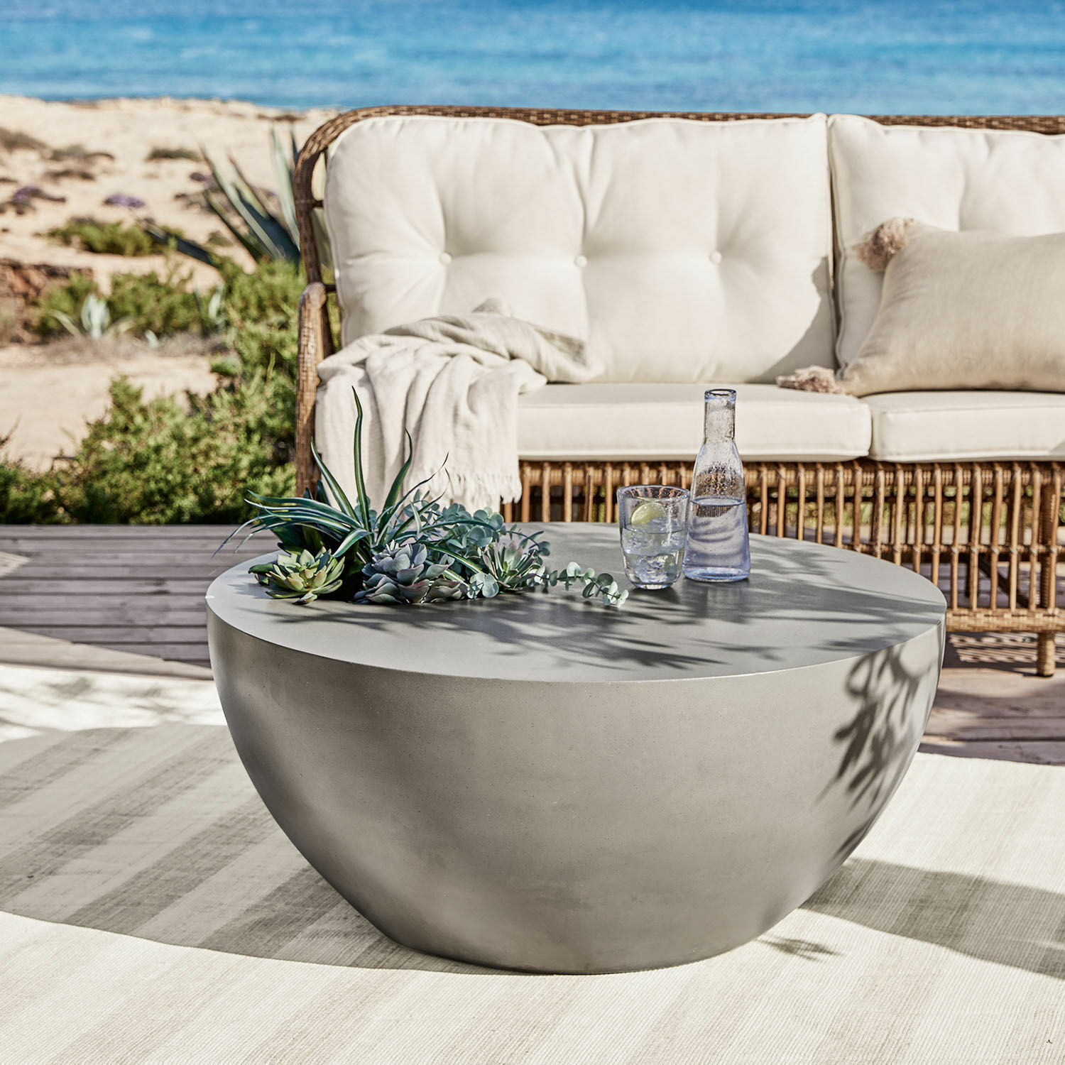 Table basse Plévin Table basse ronde en béton gris sur terrasse avec décoration de succulentes et verre d'eau