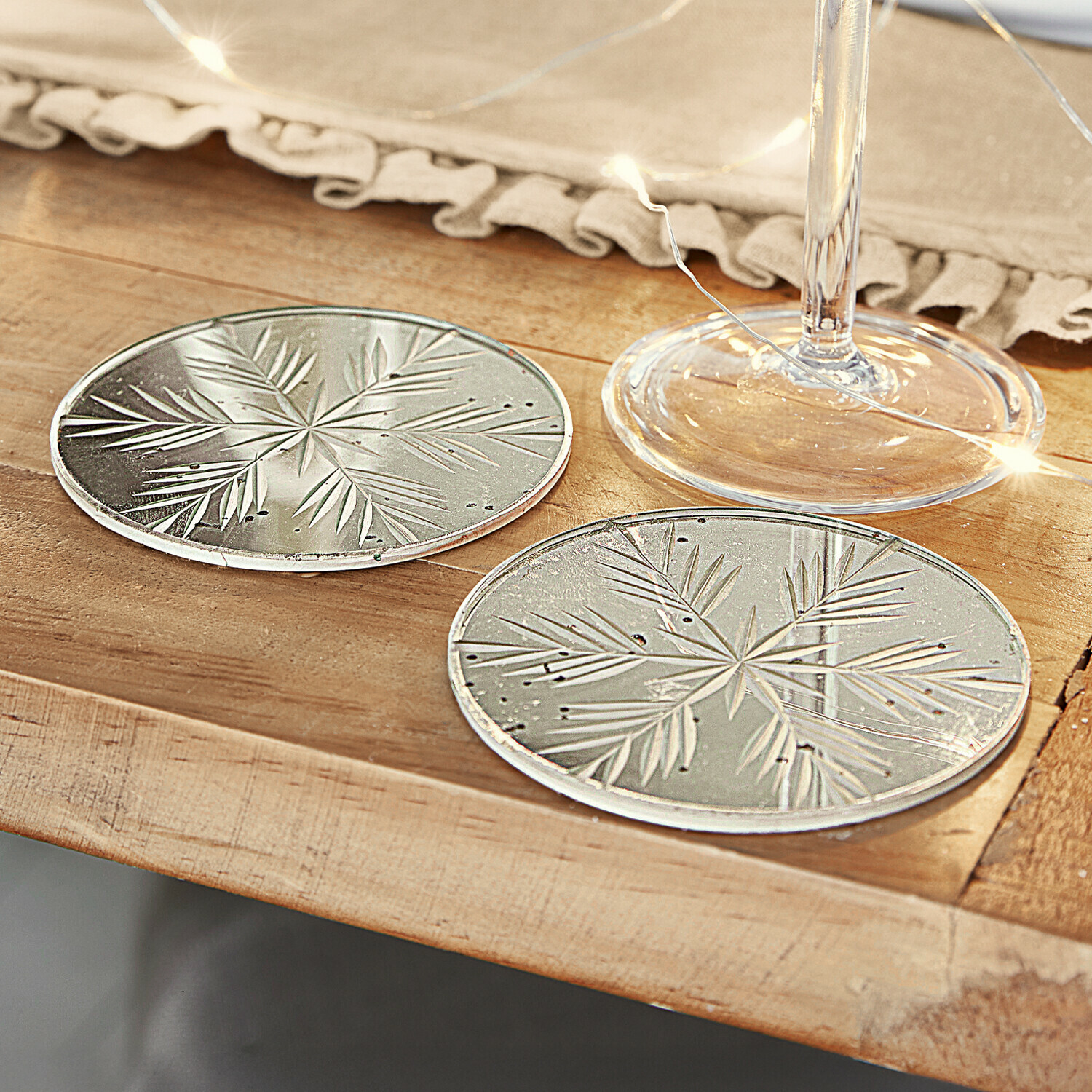 Lot de 2 dessous de verres Angeloi Sous-verres en verre gravés de motifs de feuilles sur table en bois avec guirlande lumineuse