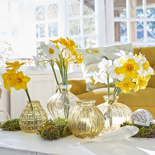 Ensemble de quatre vases en verre transparent avec fleurs jaunes et blanches sur une table claire