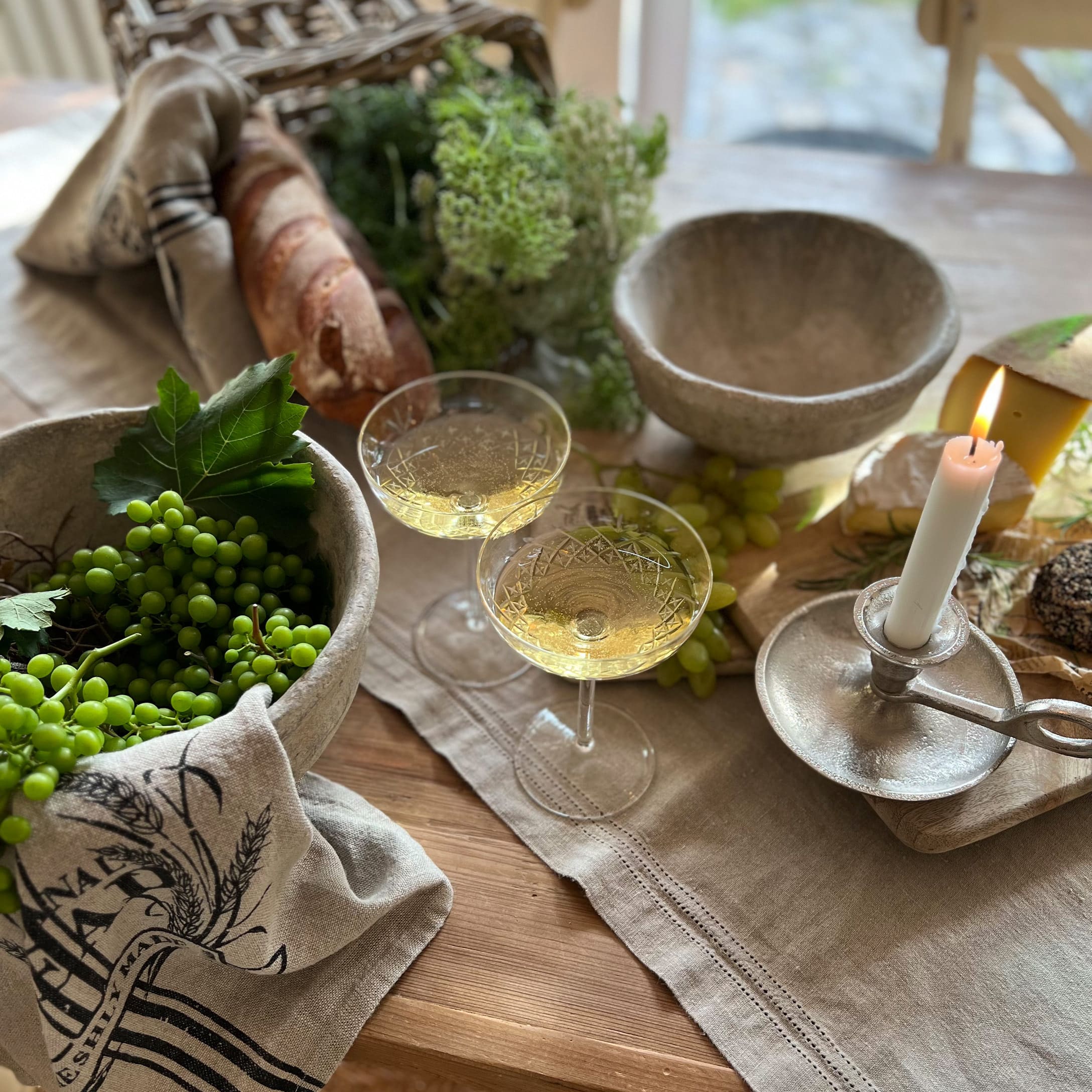 Table rustique avec bols en pierre, bougie allumée, verres de vin blanc, pain et raisins verts