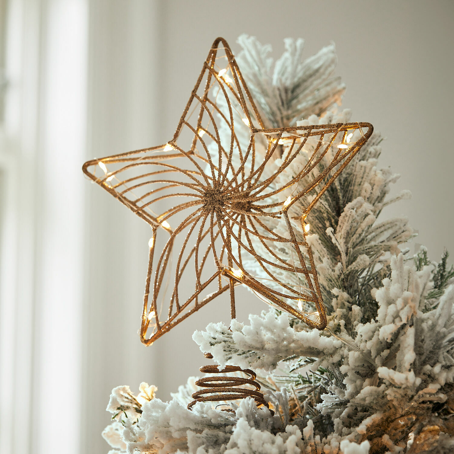 Décoration de sapin LED Pivion Étoile en métal doré avec lumières LED sur un sapin artificiel blanc enneigé pour décoration de Noël