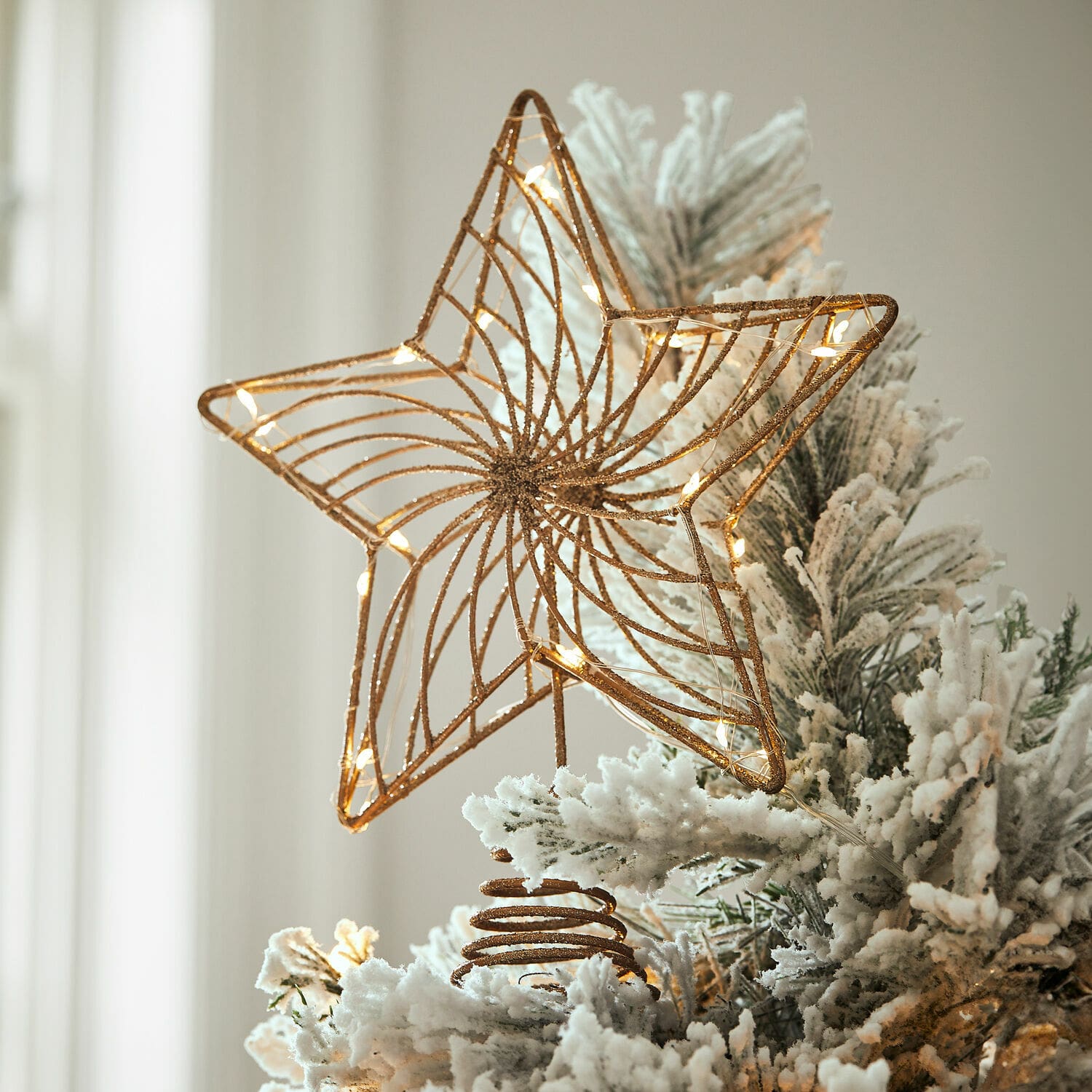 Décoration de sapin LED Pivion Étoile en métal doré avec lumières LED sur un sapin artificiel blanc enneigé pour décoration de Noël