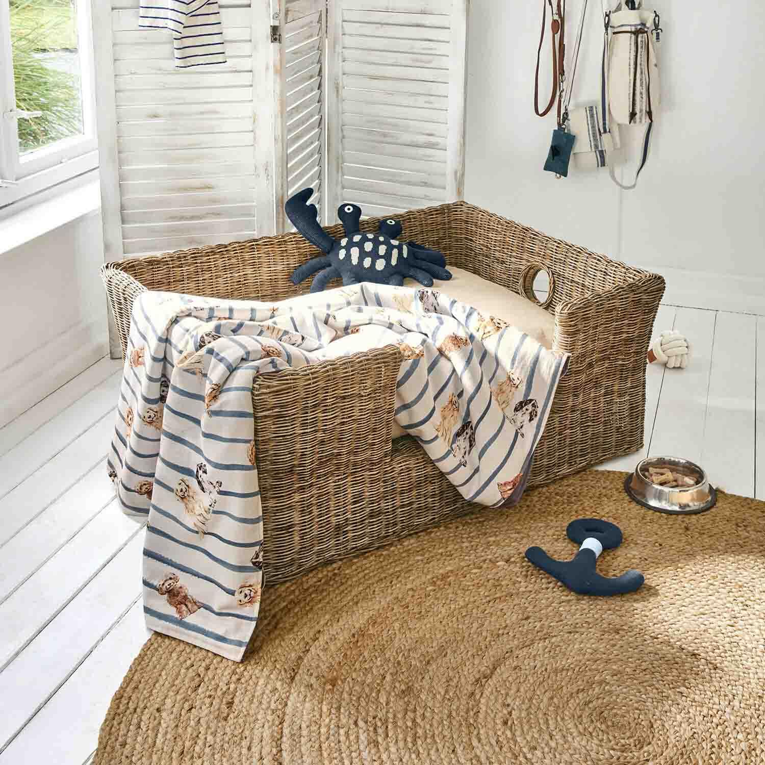 Panier en osier pour chien avec coussin beige, couverture rayée à motif chiens, jouets et gamelle