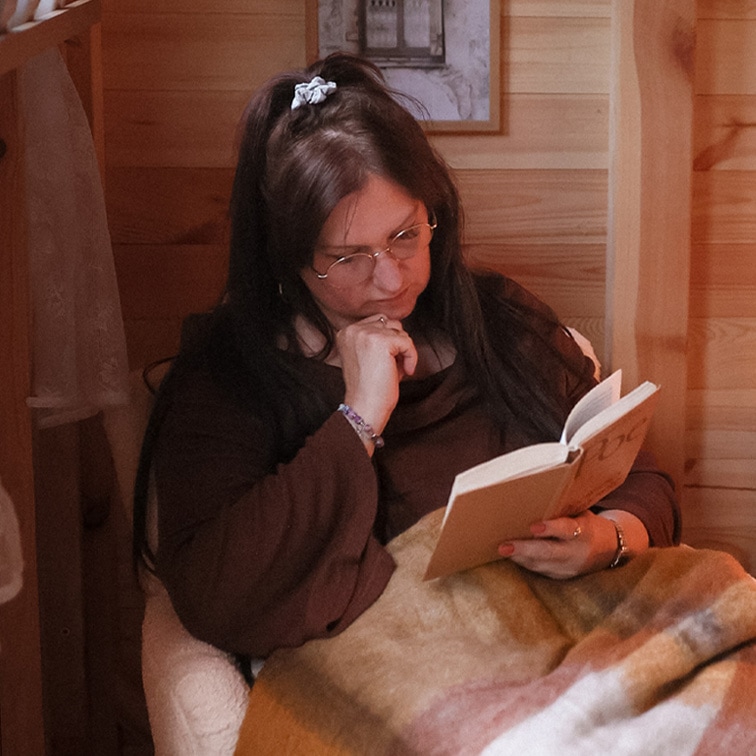 Femme lisant un livre sous une couverture douce multicolore dans un intérieur en bois, moment de détente