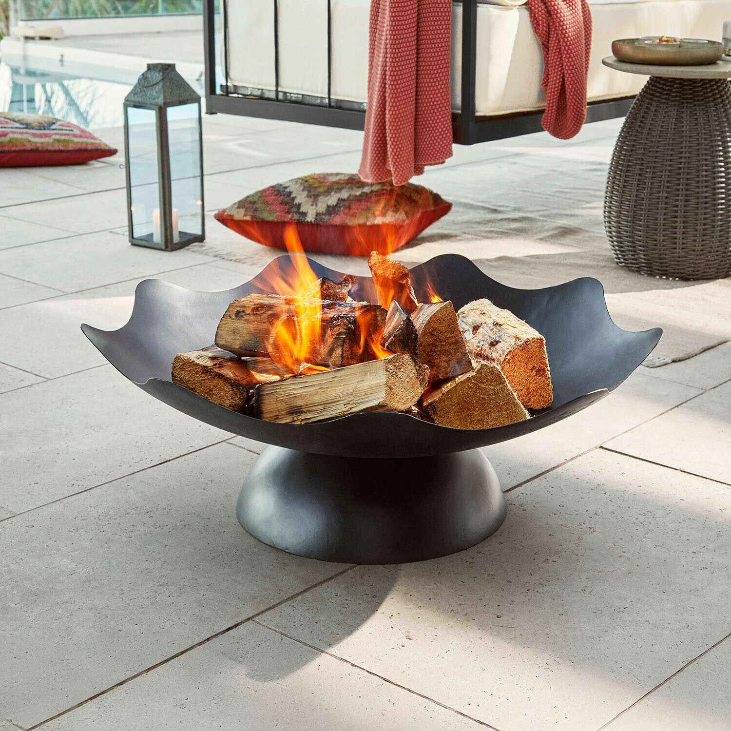 Brasero Ironwell Brasero en métal noir avec bûches en feu sur terrasse, parfait pour jardin et détente extérieure