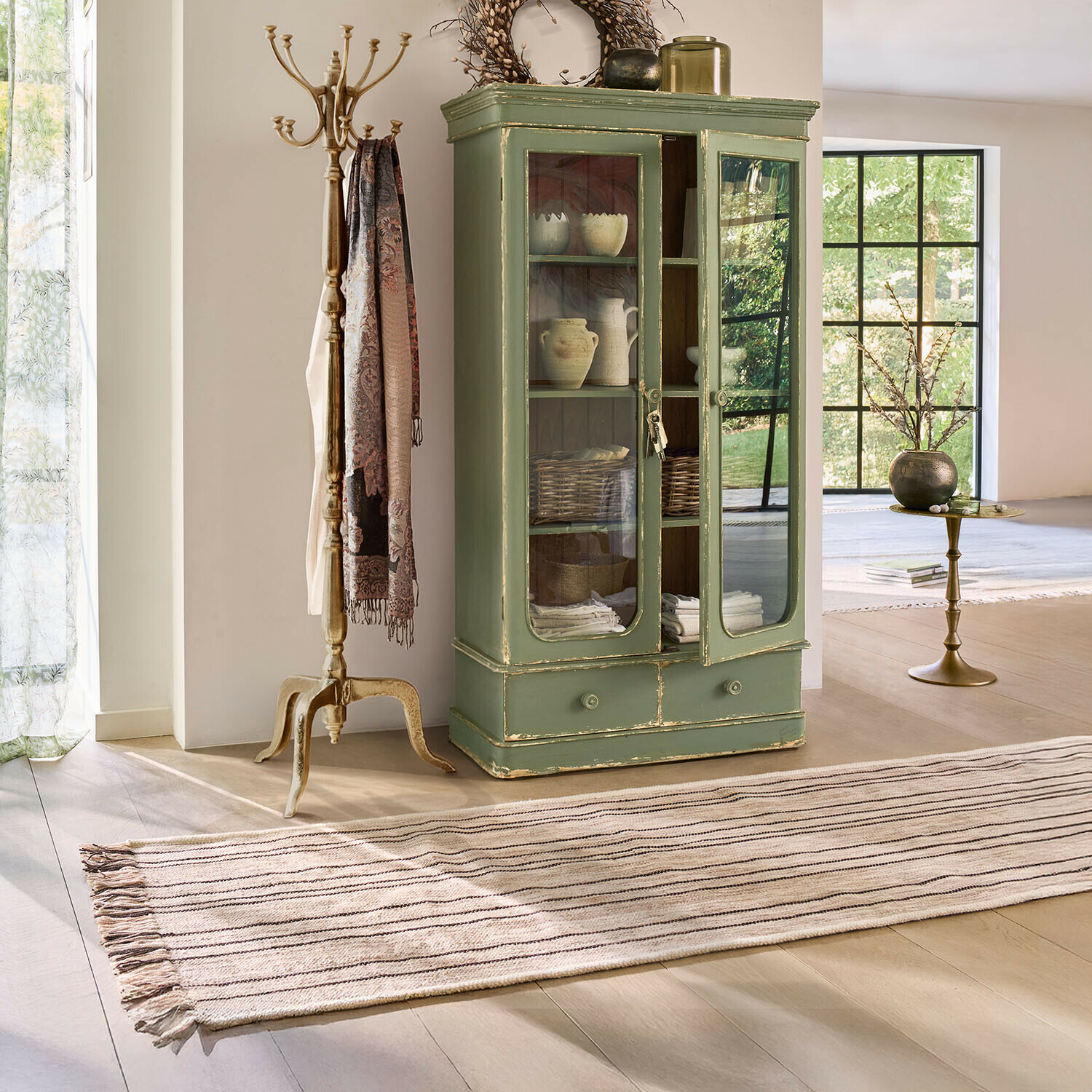Tapis long Brisalda Vitrine en bois vert avec portes vitrées et tiroir dans un salon lumineux au style vintage