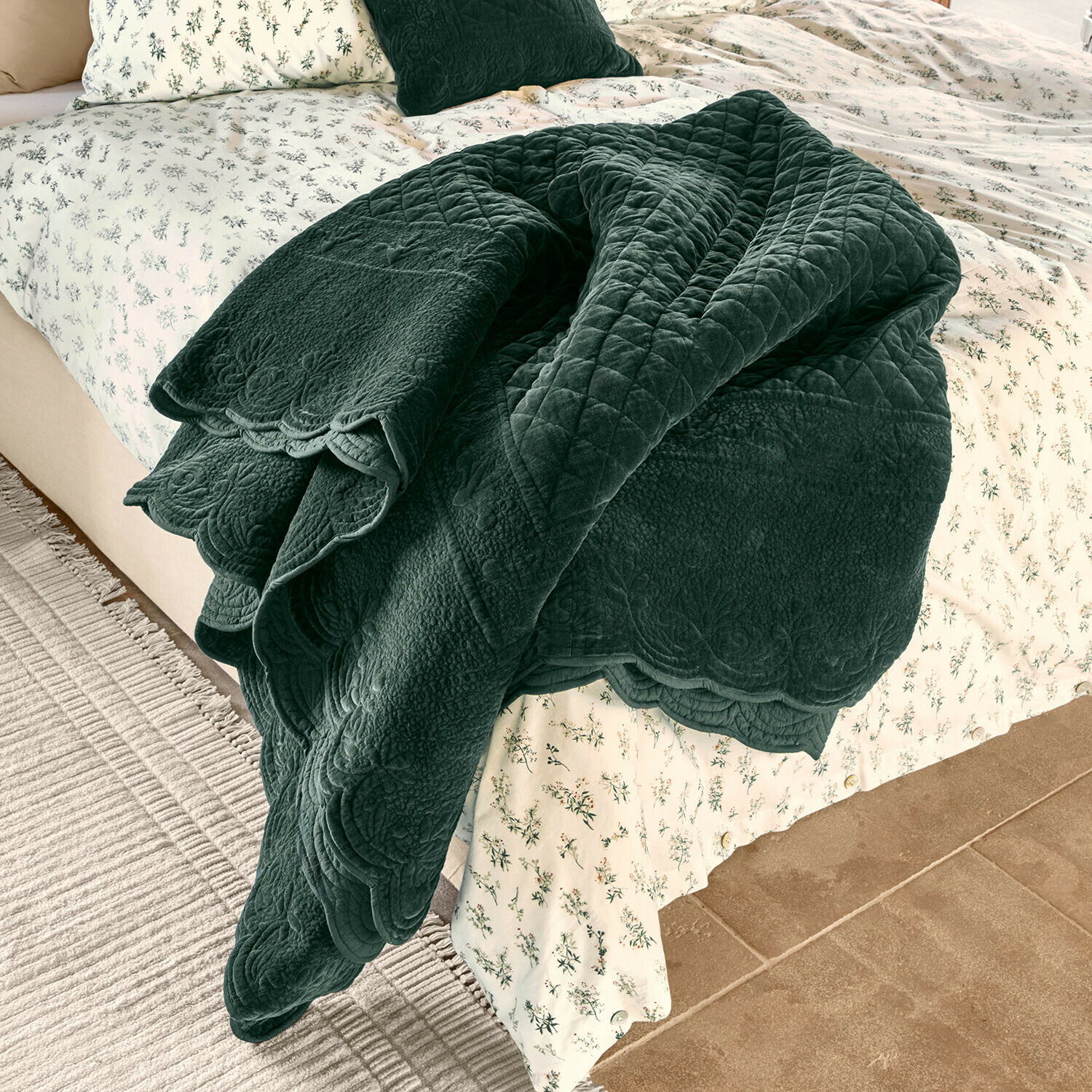 Courtepointe Lunévois Plaid matelassé vert foncé en tissu doux posé sur un lit avec une literie claire à motifs floraux