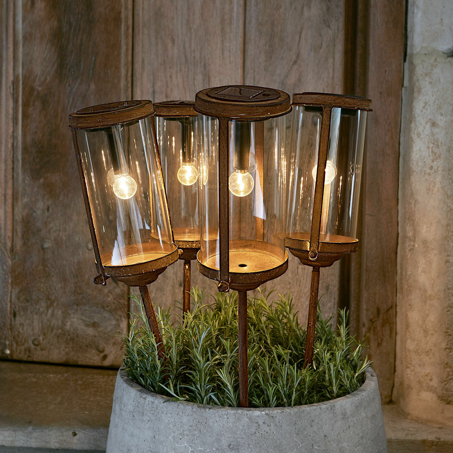 Lanterne solaire Ensemble de quatre lanternes de jardin rouillées avec abat-jours en verre et lumière LED chaude dans un pot en béton