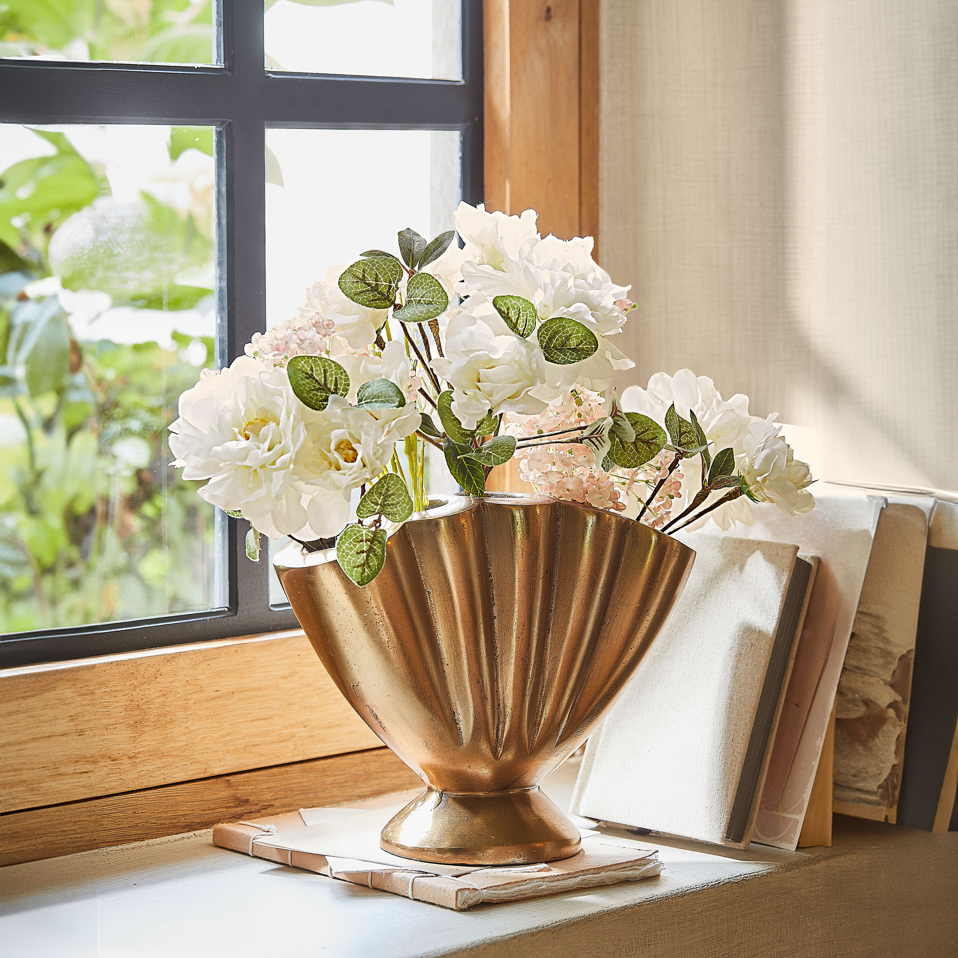 Vase doré en métal en forme d'éventail avec fleurs blanches sur le rebord de la fenêtre