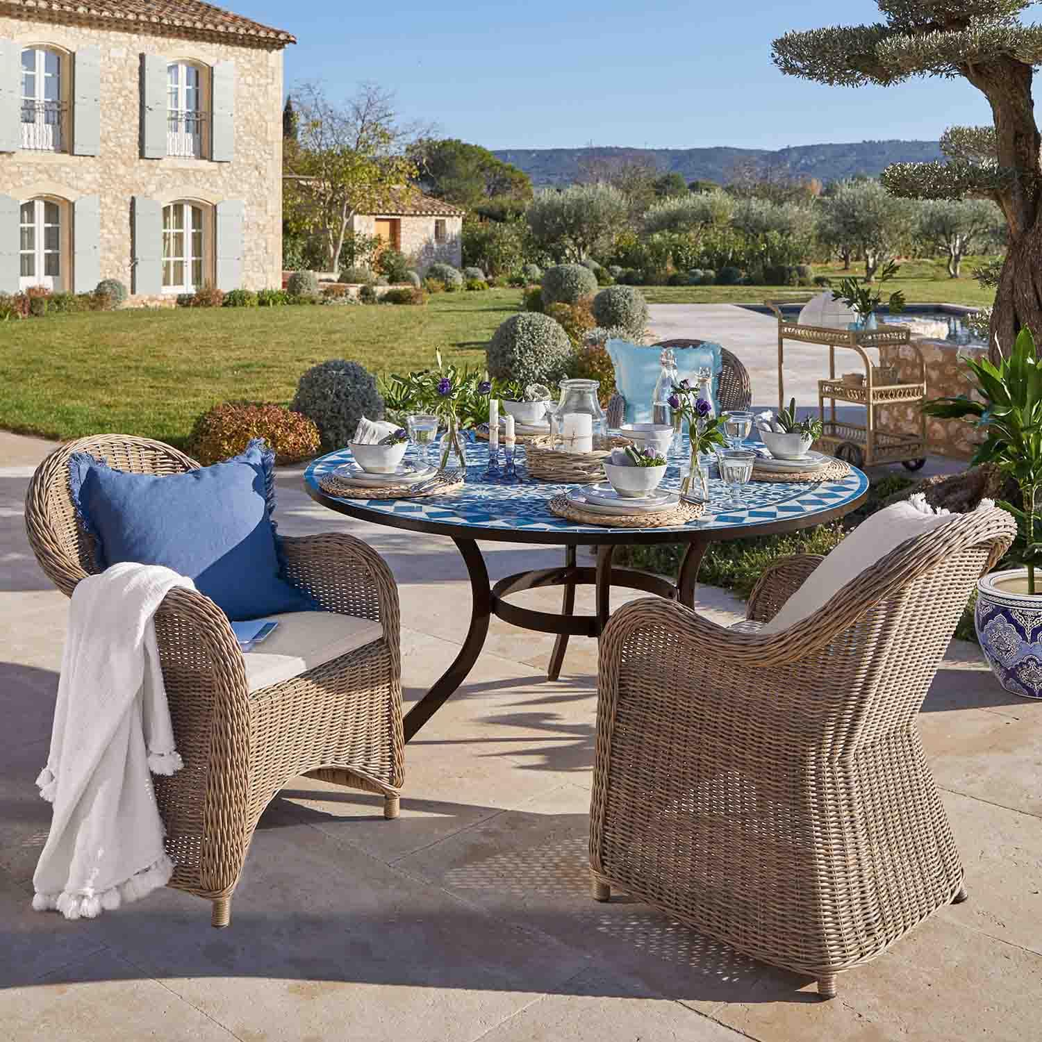 Table ronde en mosaïque bleue avec chaises en rotin beige sur terrasse ensoleillée de jardin