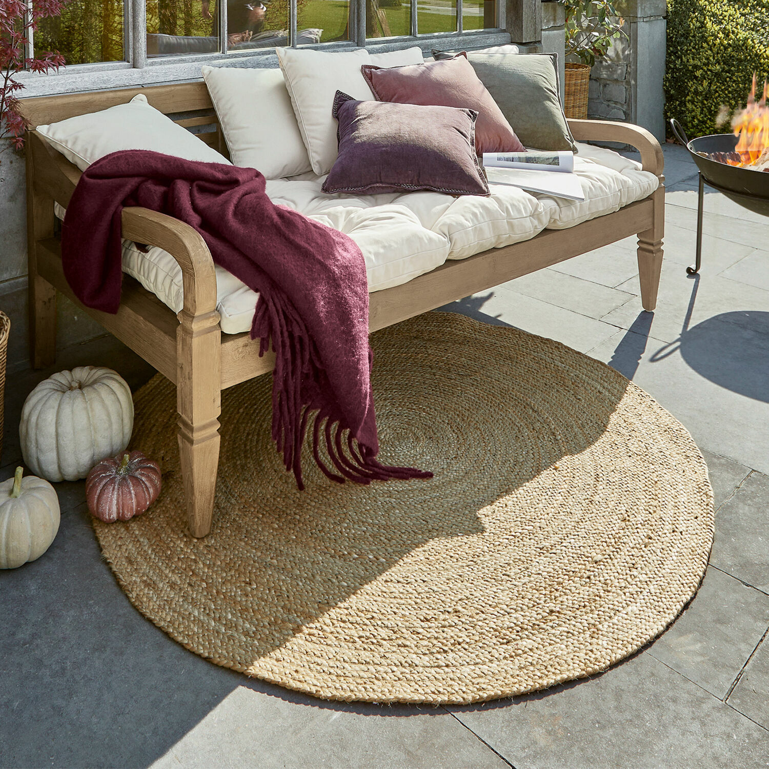 Tapis Imene Tapis rond en jute couleur naturelle sous un banc en bois avec coussins et plaid bordeaux