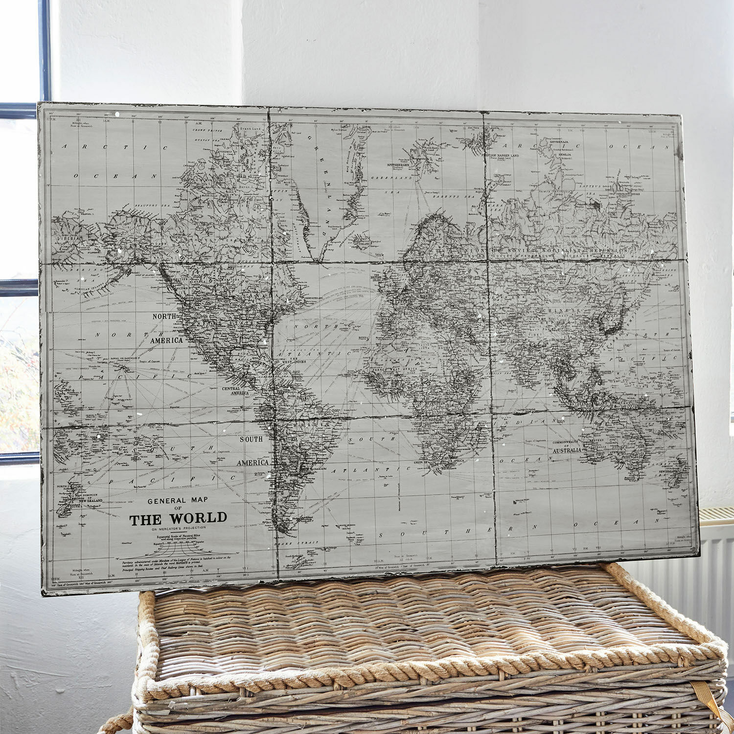Tableau Macolin Carte du monde vintage en tons gris posée sur un panier en osier pour décoration intérieure