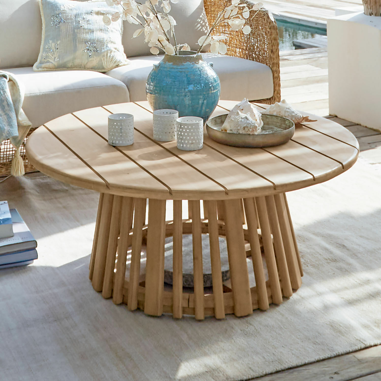 Table basse FSC®-100% Tewsbury Table basse ronde en bois clair avec décorations sur une terrasse ensoleillée près de la piscine
