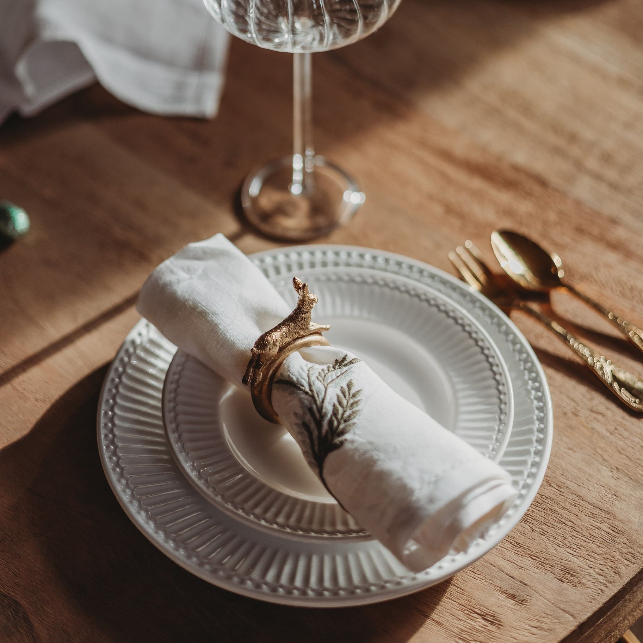 Assiette en céramique blanche avec serviette ornée et rond de serviette doré sur table en bois
