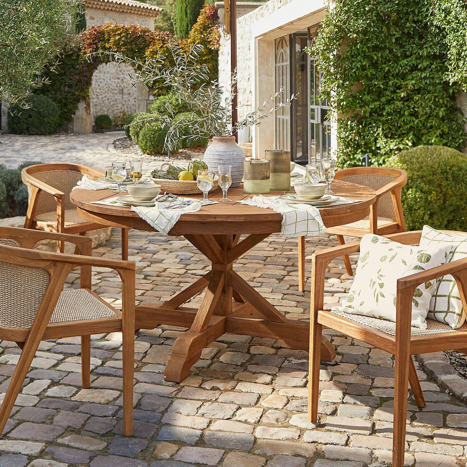 Table Wendreau Table ronde et chaises en teck sur patio pavé avec décorations et vaisselle pour repas en extérieur
