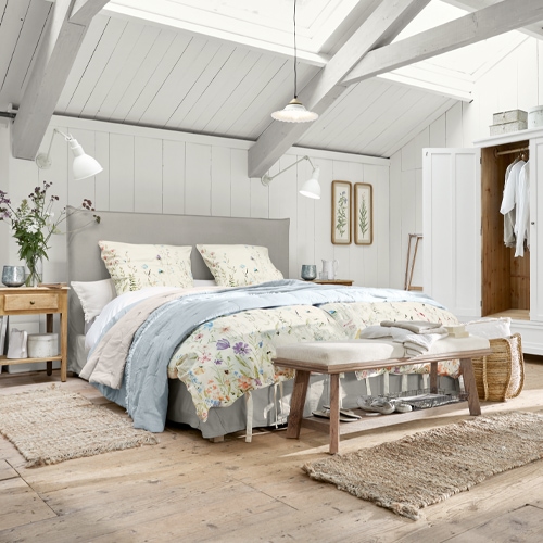 Chambre chaleureuse avec lit gris clair, literie florale, bois naturel et tapis en fibres naturelles
