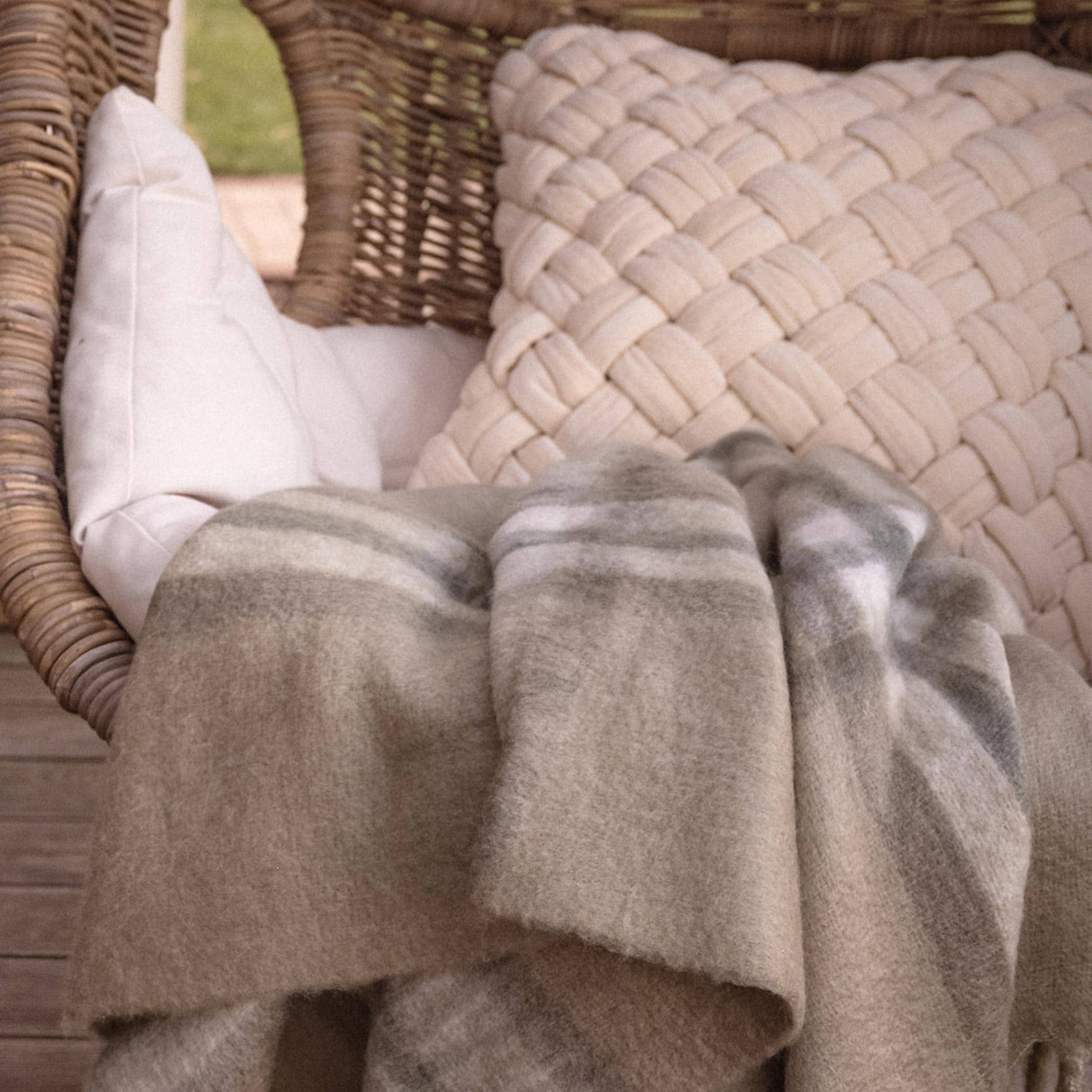 Plaid beige doux à rayures posé sur un fauteuil en osier avec coussins sur la terrasse