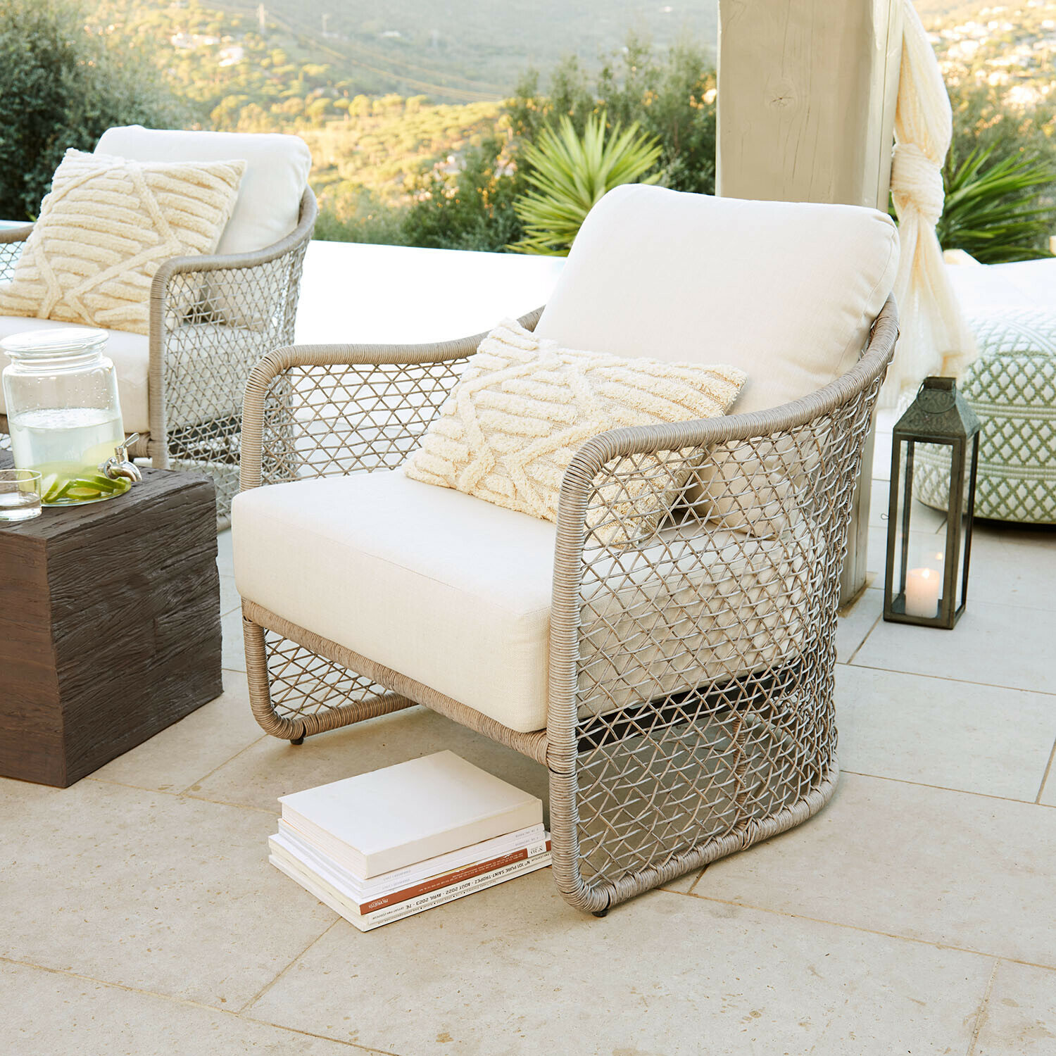 Fauteuil Langforda Fauteuil d'extérieur en rotin beige avec coussin crème sur terrasse avec vue sur la nature