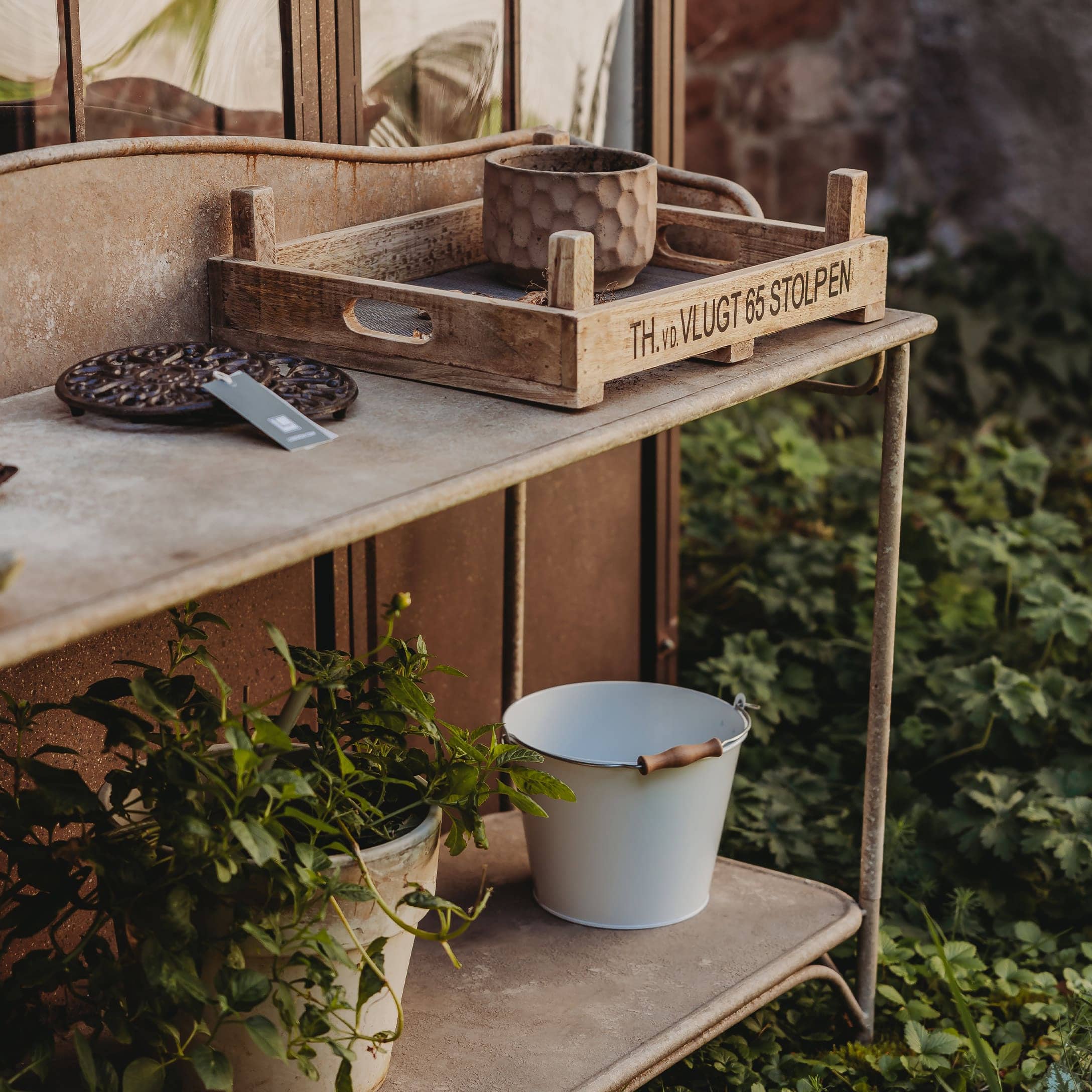 Plateau en bois décoratif sur une table en métal avec pot de fleurs et seau blanc dans un jardin