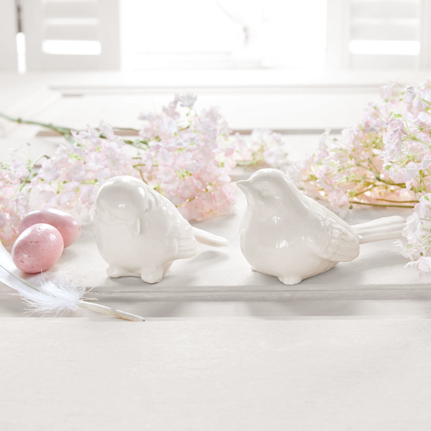 Deux figurines d'oiseaux en céramique blanche sur fond clair avec fleurs roses et œufs décoratifs