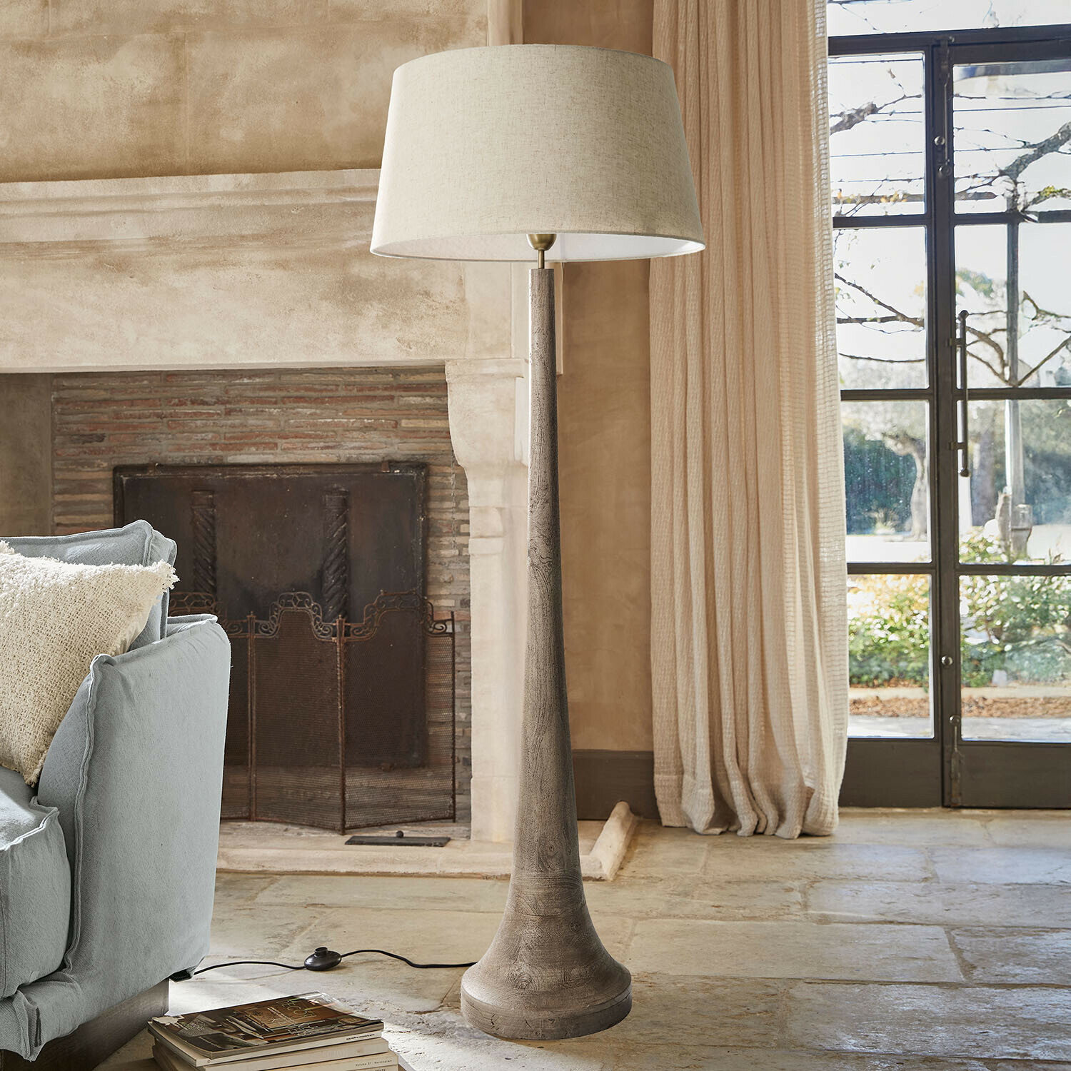 Lampadaire en bois avec abat-jour beige dans un salon chaleureux avec cheminée et canapé bleu