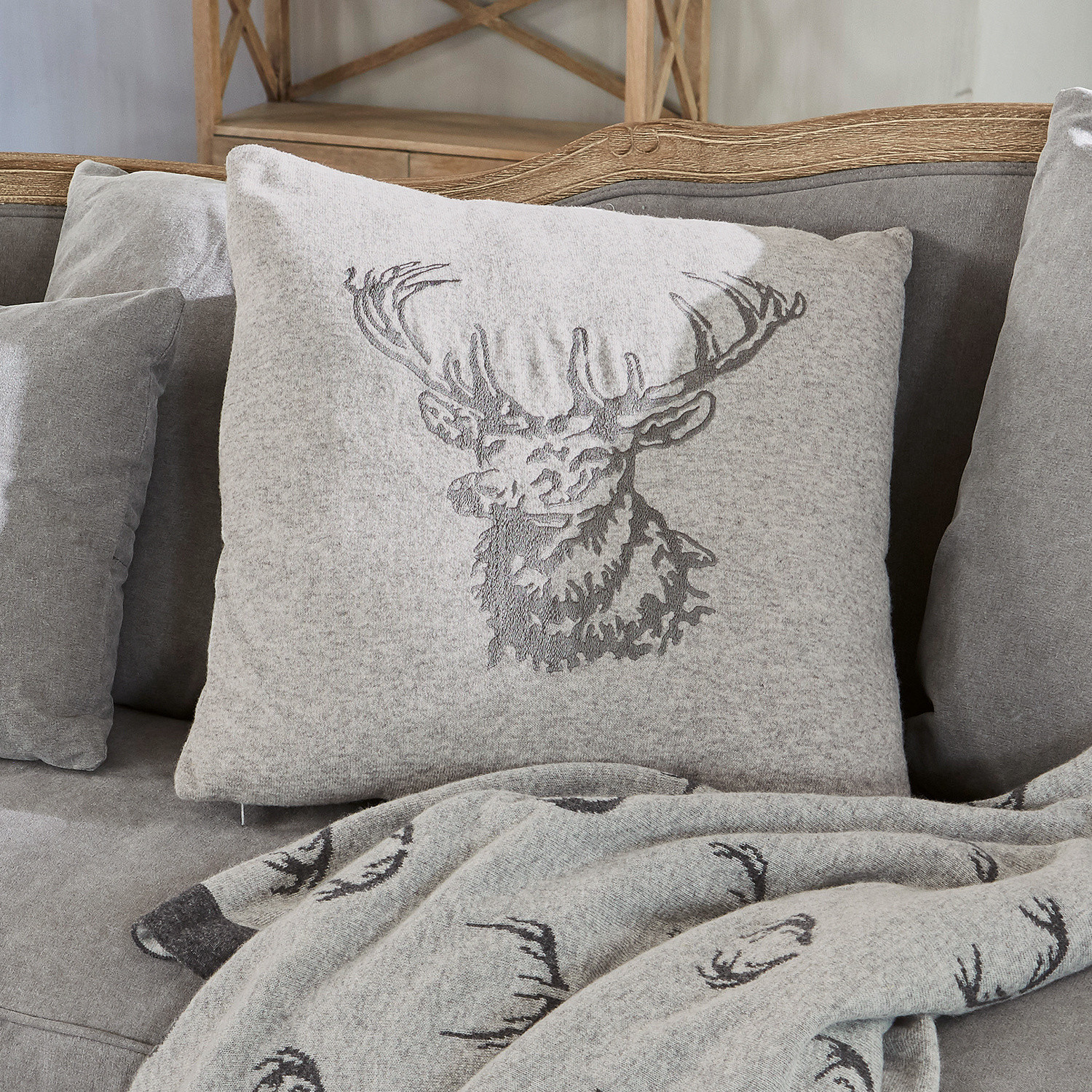 Housse de coussin Dario Coussin gris en tissu doux avec motif cerf sur canapé gris avec plaid assorti à motif cerf